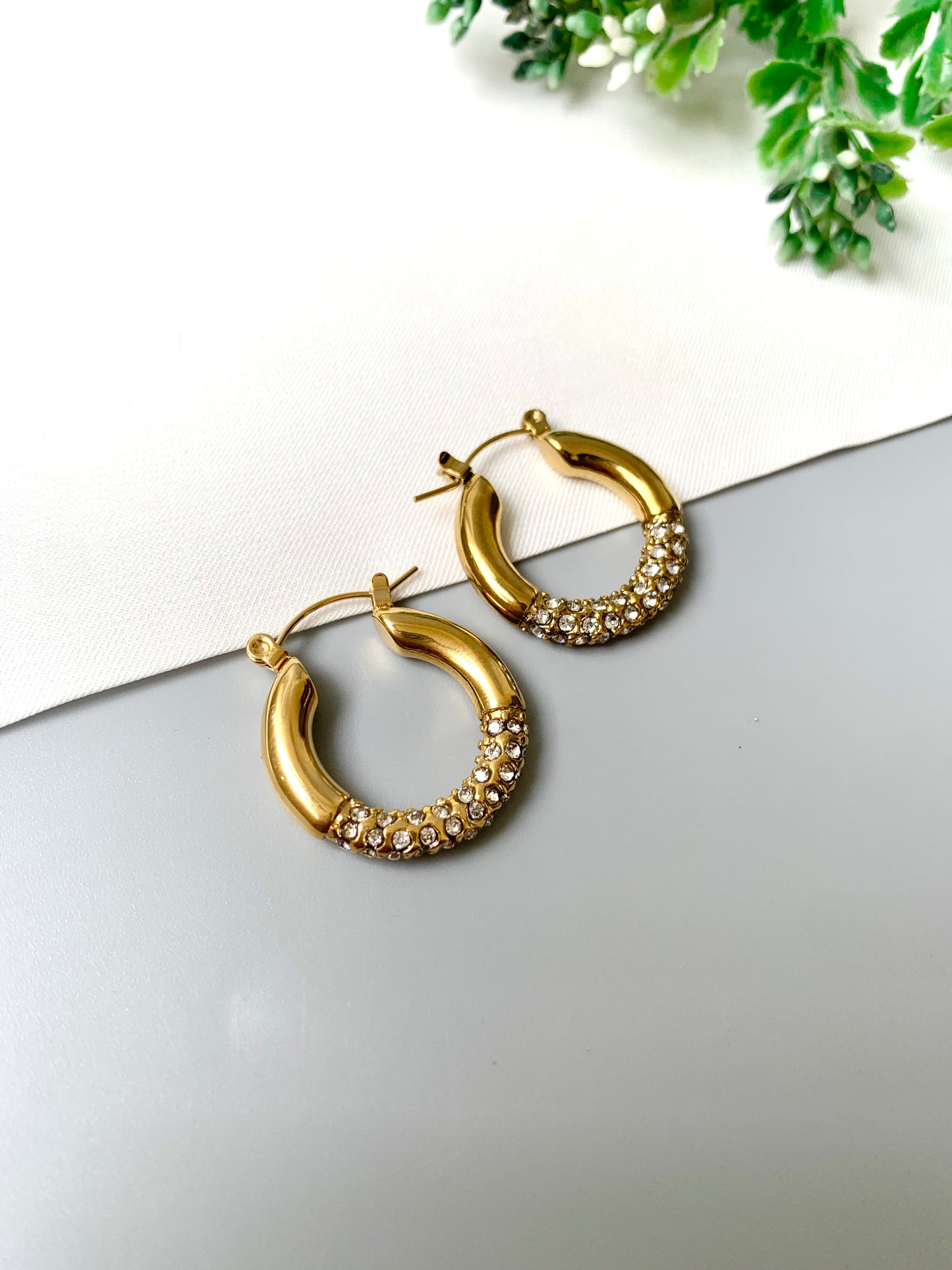 Gold-plated stainless steel crystal-accented hoop earrings with a sleek, classic design, laid out on a neutral background.