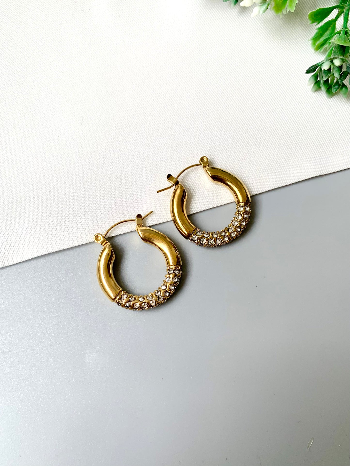 Gold-plated stainless steel crystal-accented hoop earrings with a sleek, classic design, laid out on a neutral background.
