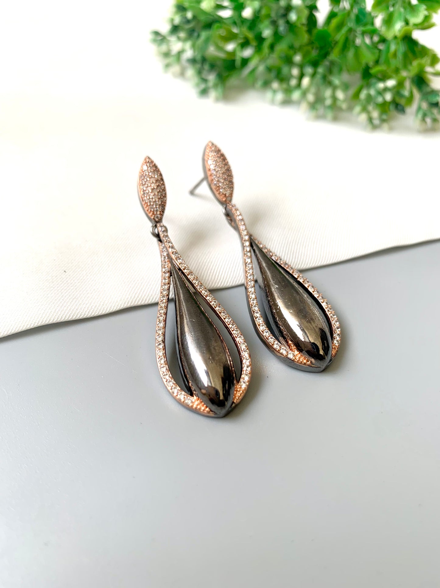 Teardrop-shaped earrings with rose gold accents on a white surface with greenery in the background