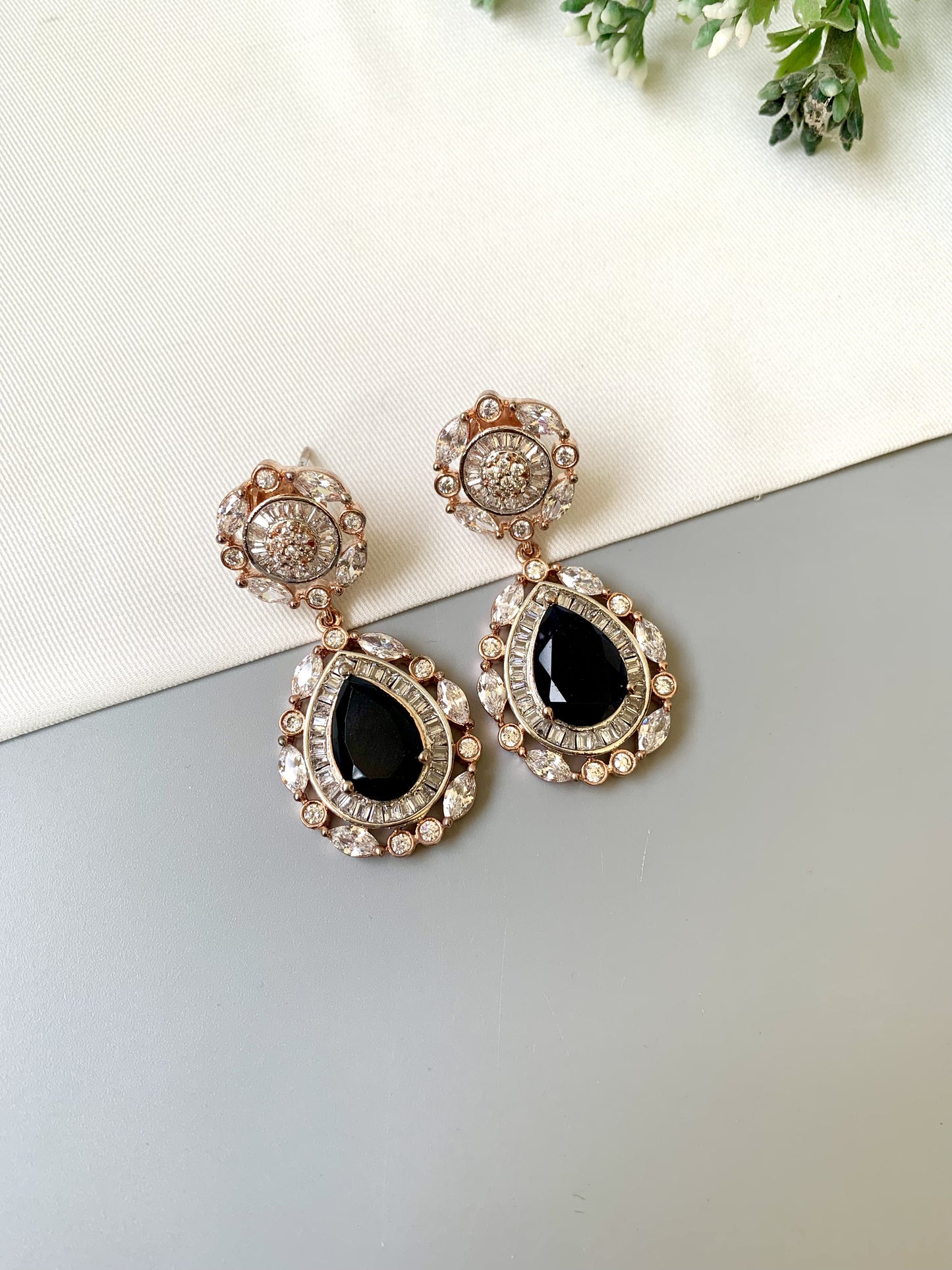 Pair of earrings with black gemstones and rose gold accents on a light surface.