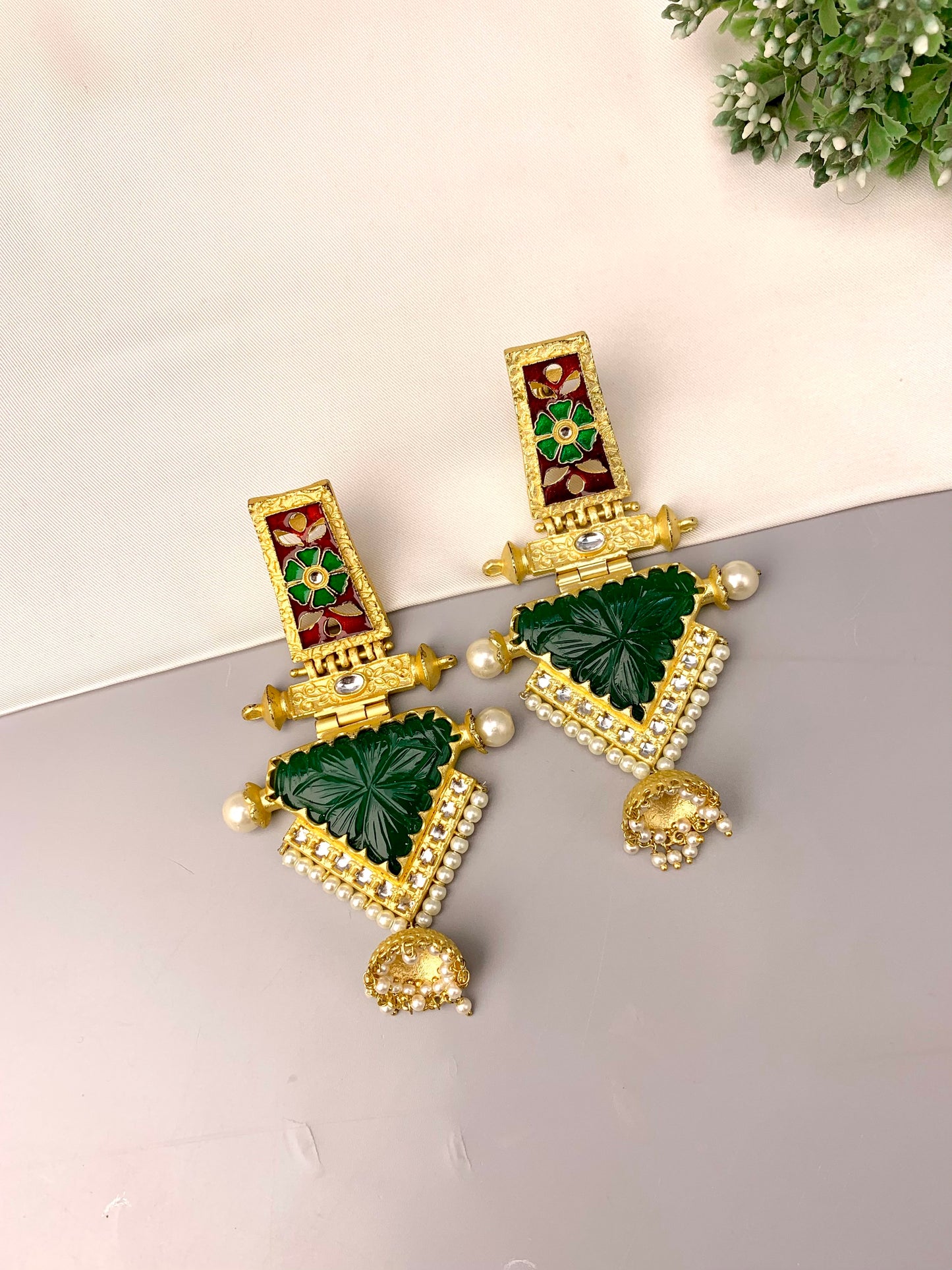 Gold and green earrings on a light surface with a plant in the background