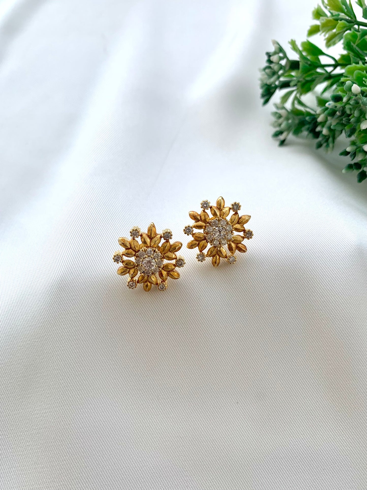 Gold floral earrings on a white fabric background with greenery.