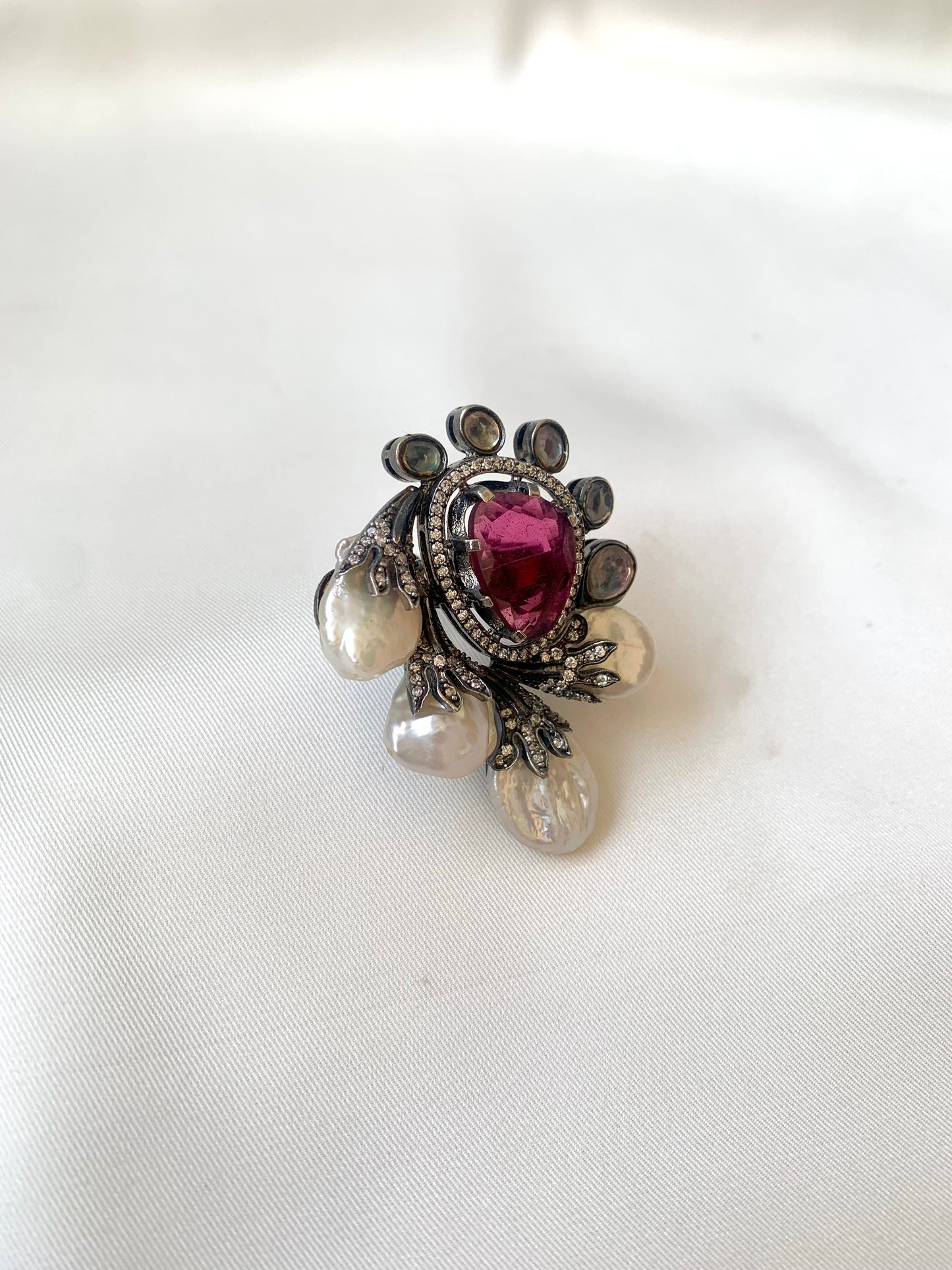 Decorative ring with a central red gemstone and pearl-like elements on a white background