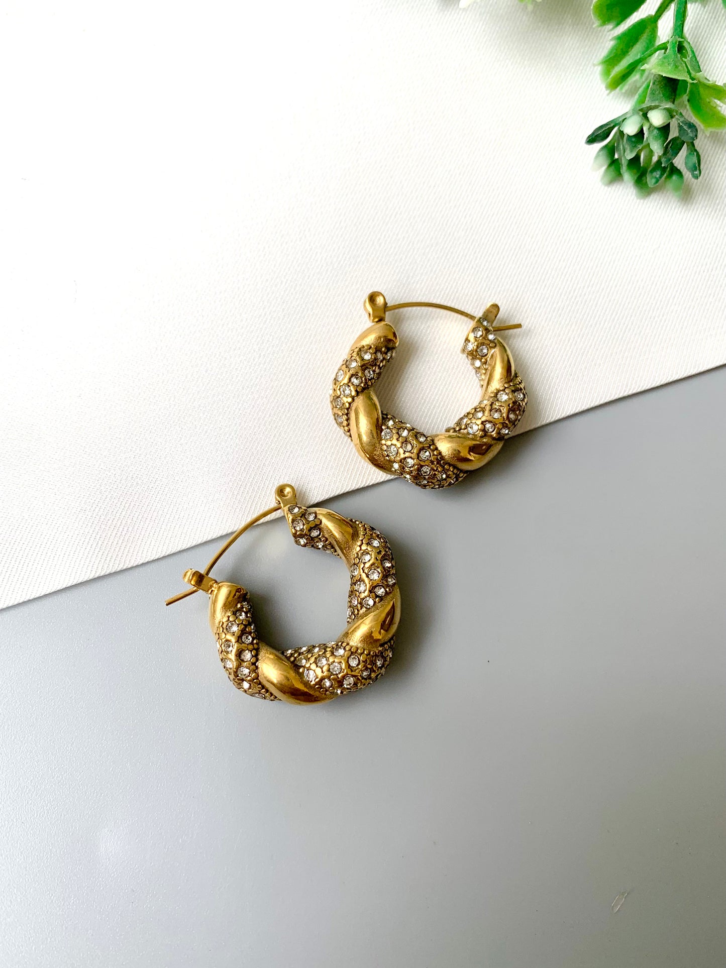 Handcrafted gold twisted hoop earrings with zirconia stones from Zamal Jewels on white and grey background