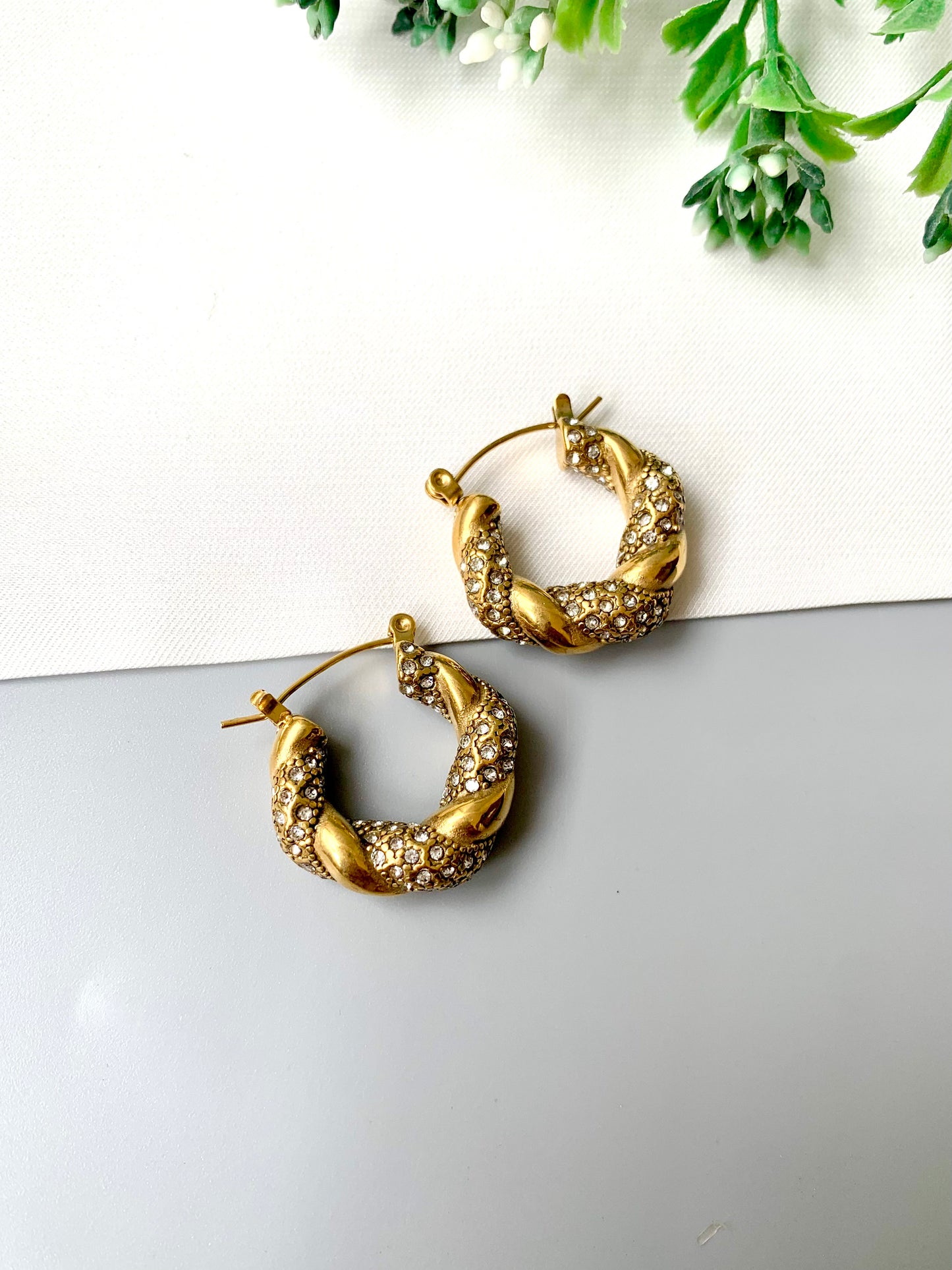 Handcrafted gold twisted hoop earrings with zirconia stones from Zamal Jewels on white and grey background