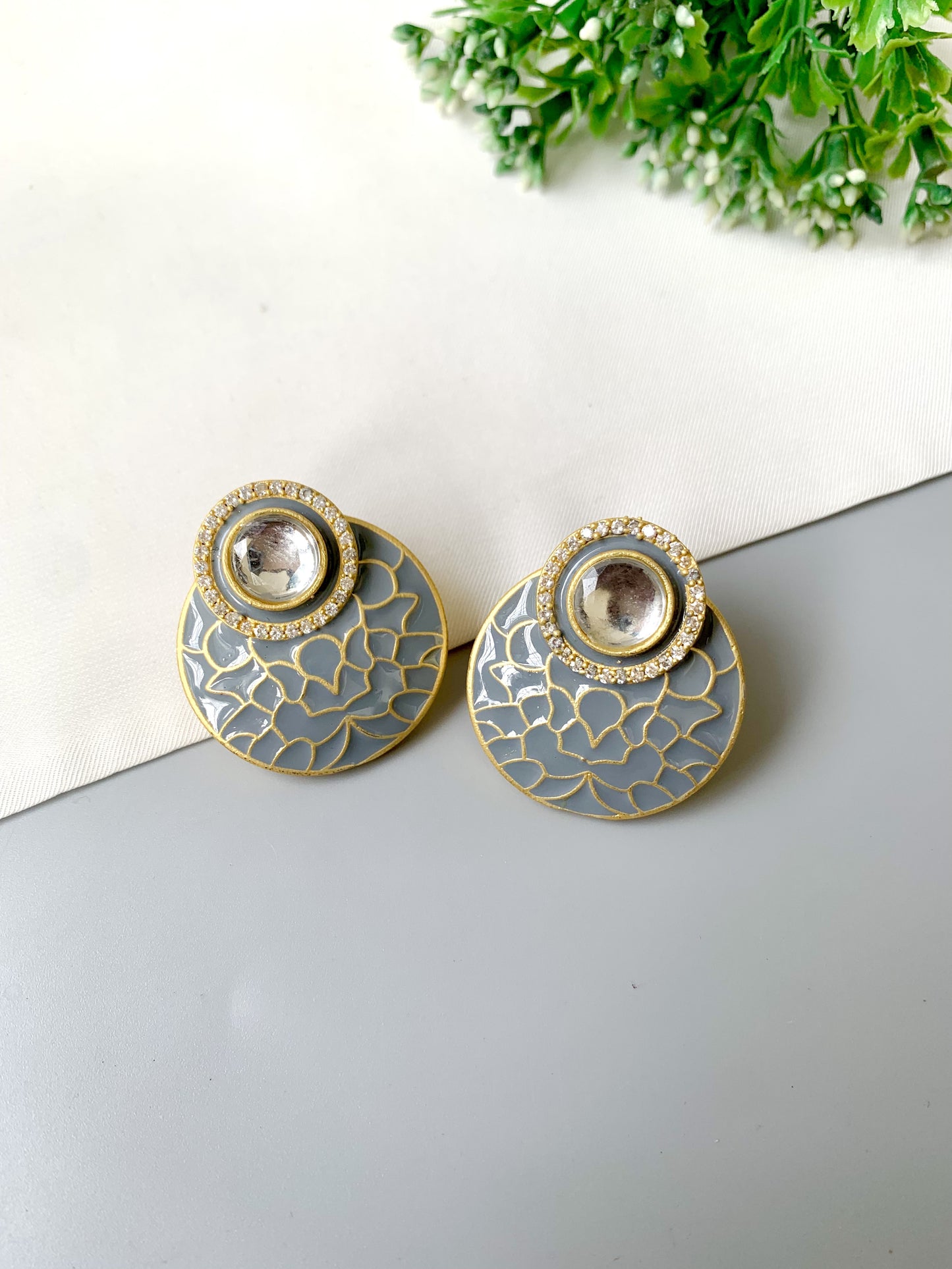 Pair of gold and gray earrings on a white surface with greenery in the background
