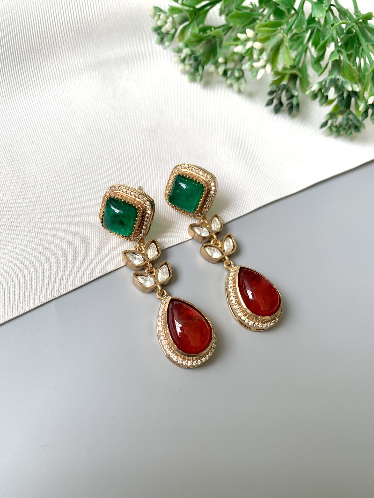 Close-up of Elayra earrings with emerald square tops, ruby teardrops and Kundan leaf design