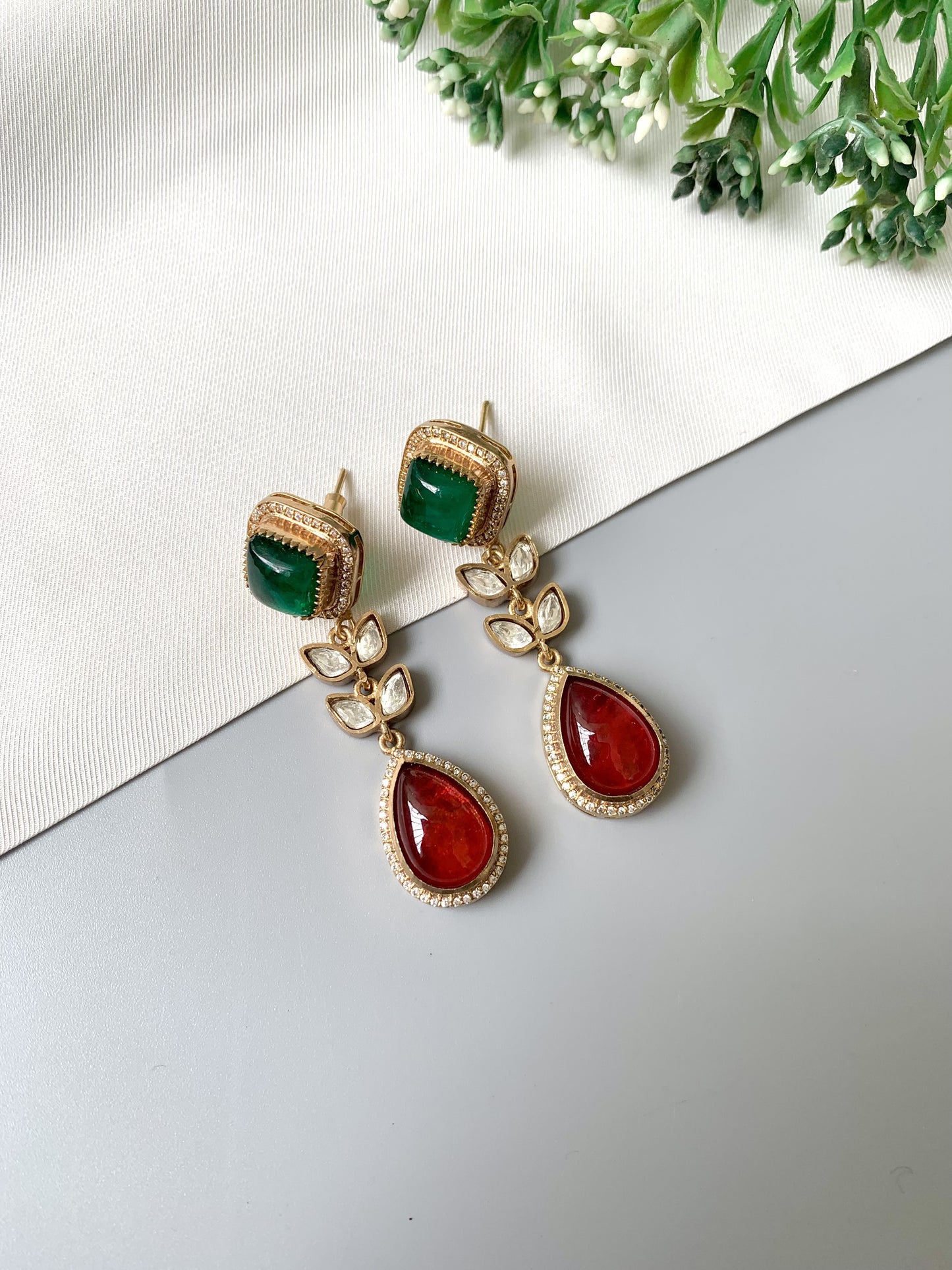 Flat lay of Elayra earrings featuring ruby and emerald stones with Polki Kundan and American Diamonds in Victorian gold