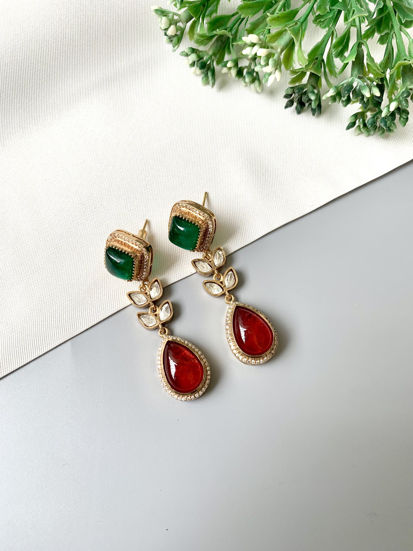 Angled view of Elayra Regal Harmony earrings with red and green stones in a gold floral setting