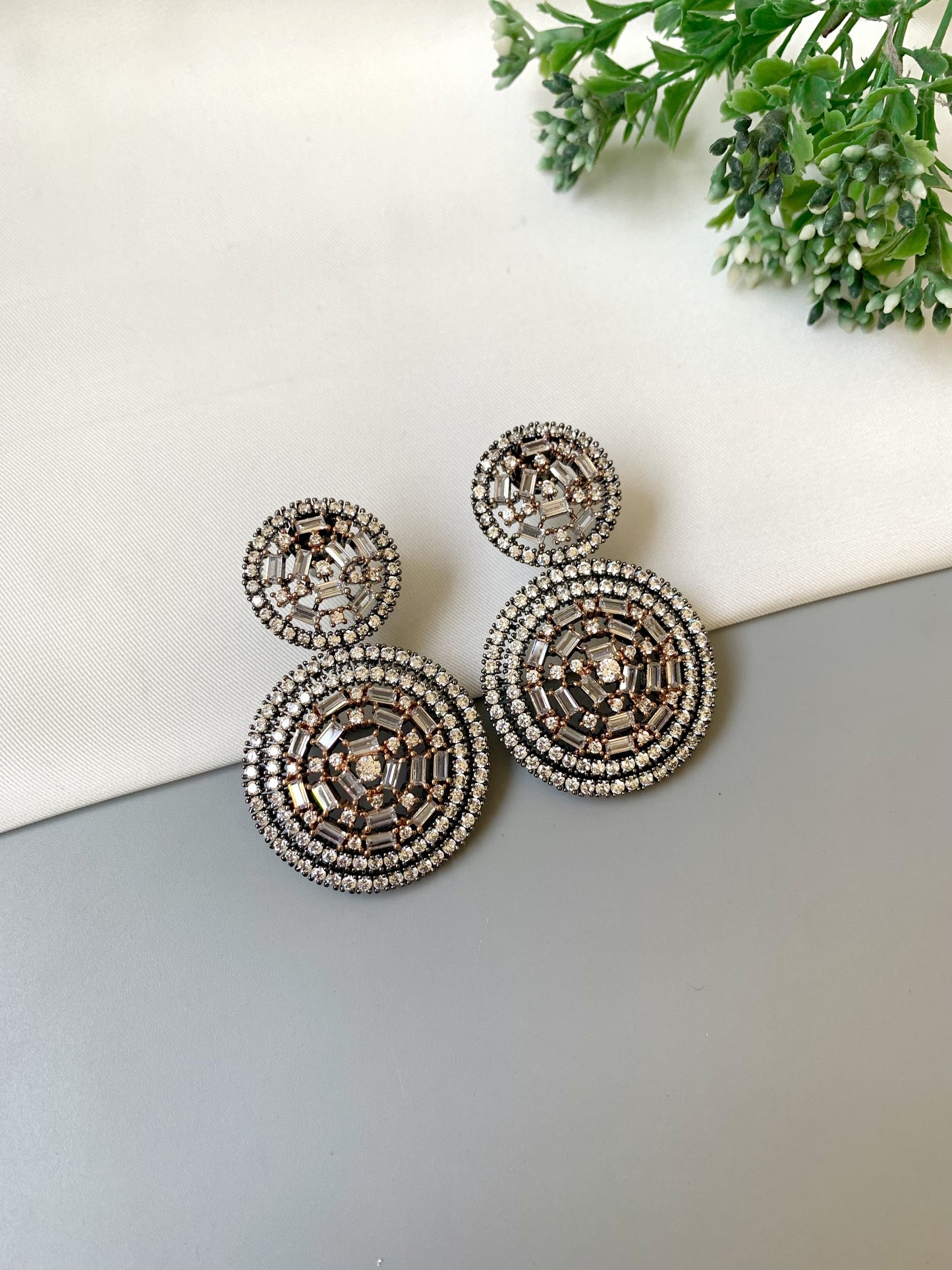 Decorative earrings on a light surface with greenery in the background