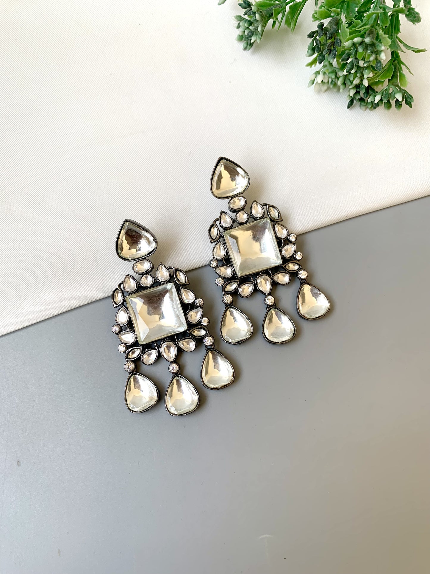 Jewelry earrings with square and teardrop shapes on a light background