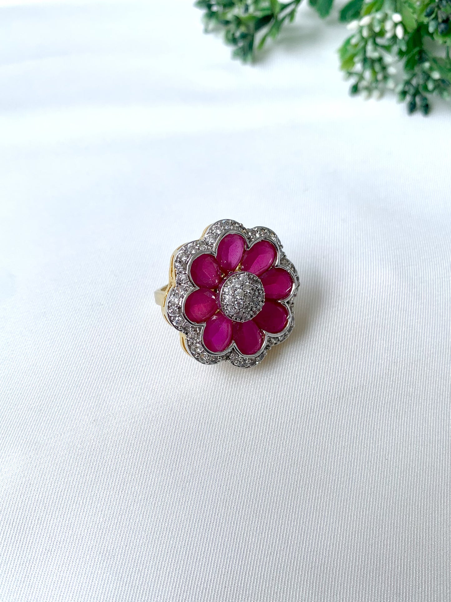 Close-up of Fiora Ruby Bloom adjustable ring featuring 22kt gold plating, semi-precious ruby petals, and American Diamond detailing on a white fabric background.