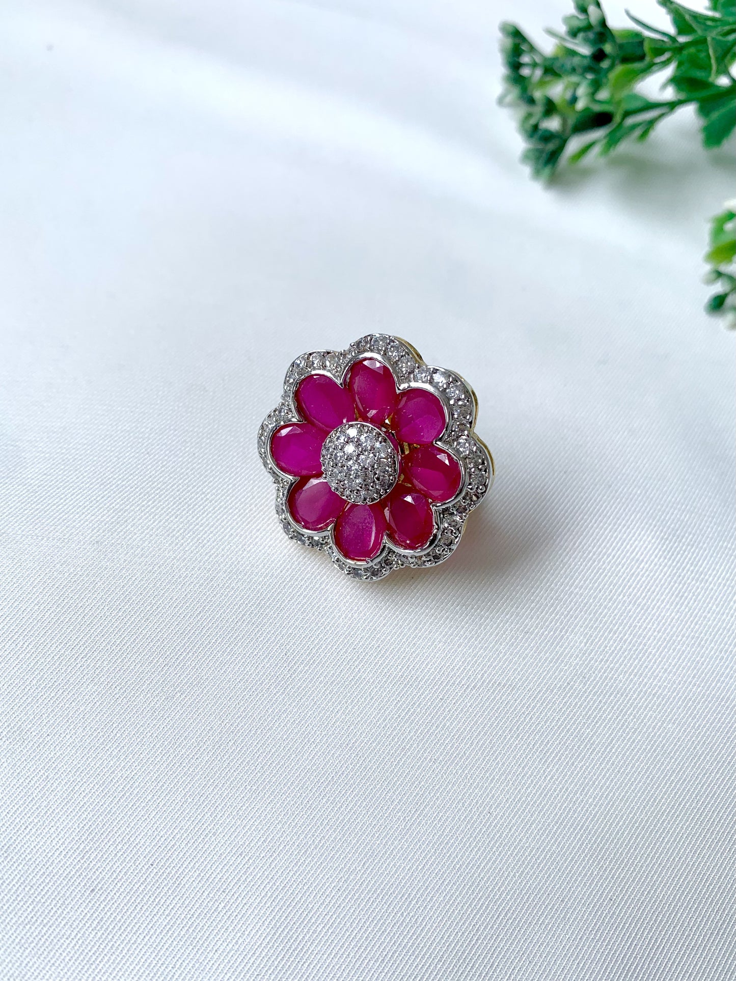 Close-up of Fiora Ruby Bloom adjustable ring featuring 22kt gold plating, semi-precious ruby petals, and American Diamond detailing on a white fabric background.
