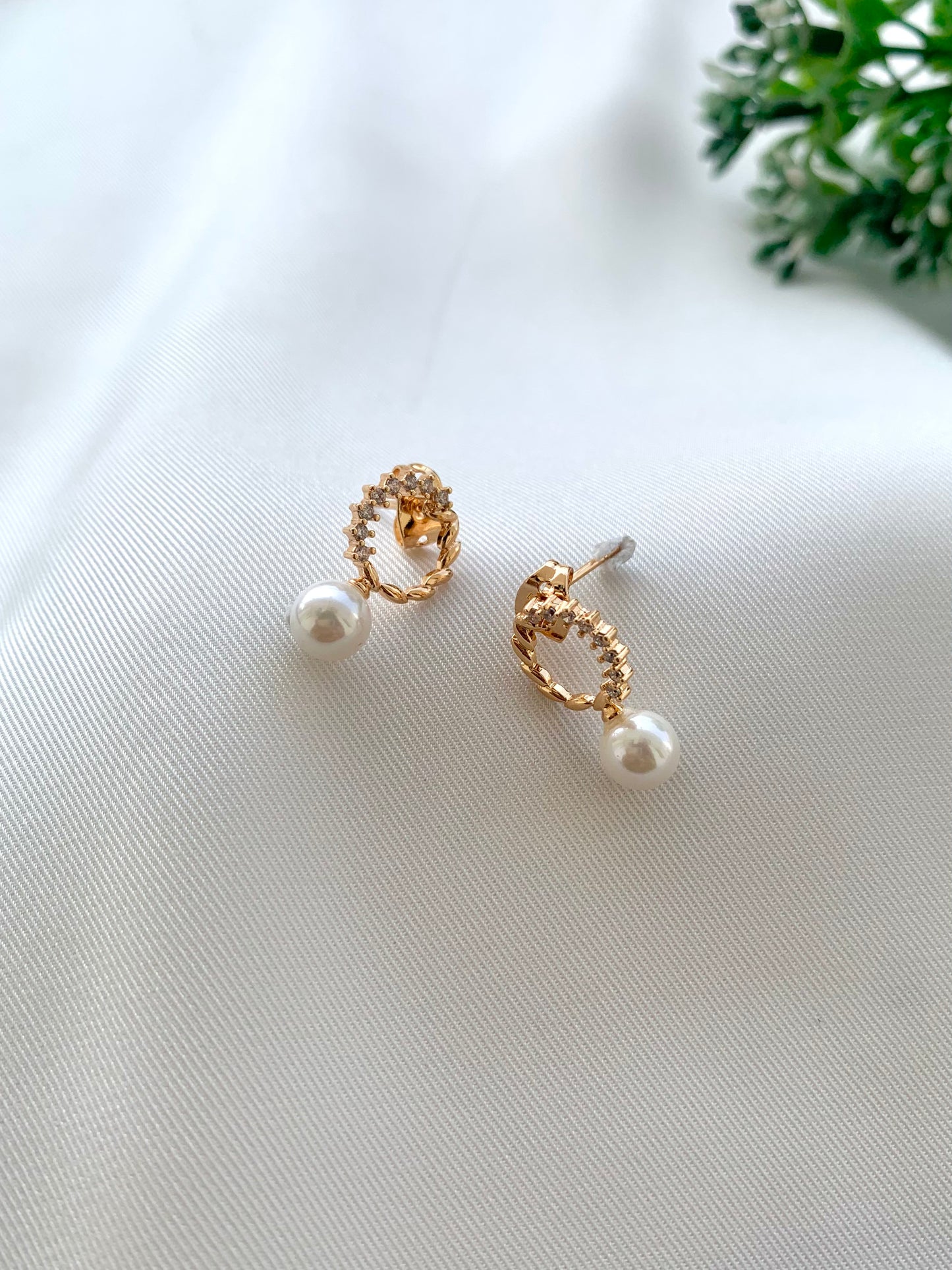 Pair of gold earrings with pearls on a white fabric background