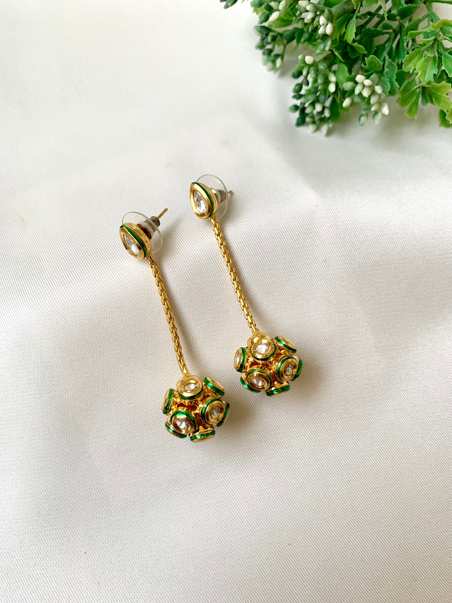 Gold and green earrings on a white fabric background with greenery.