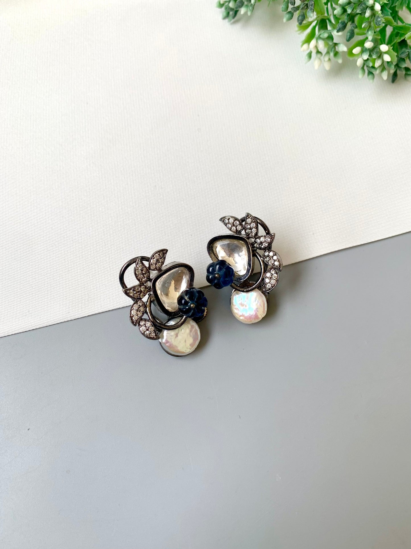 Pair of decorative earrings on a white surface with greenery in the background