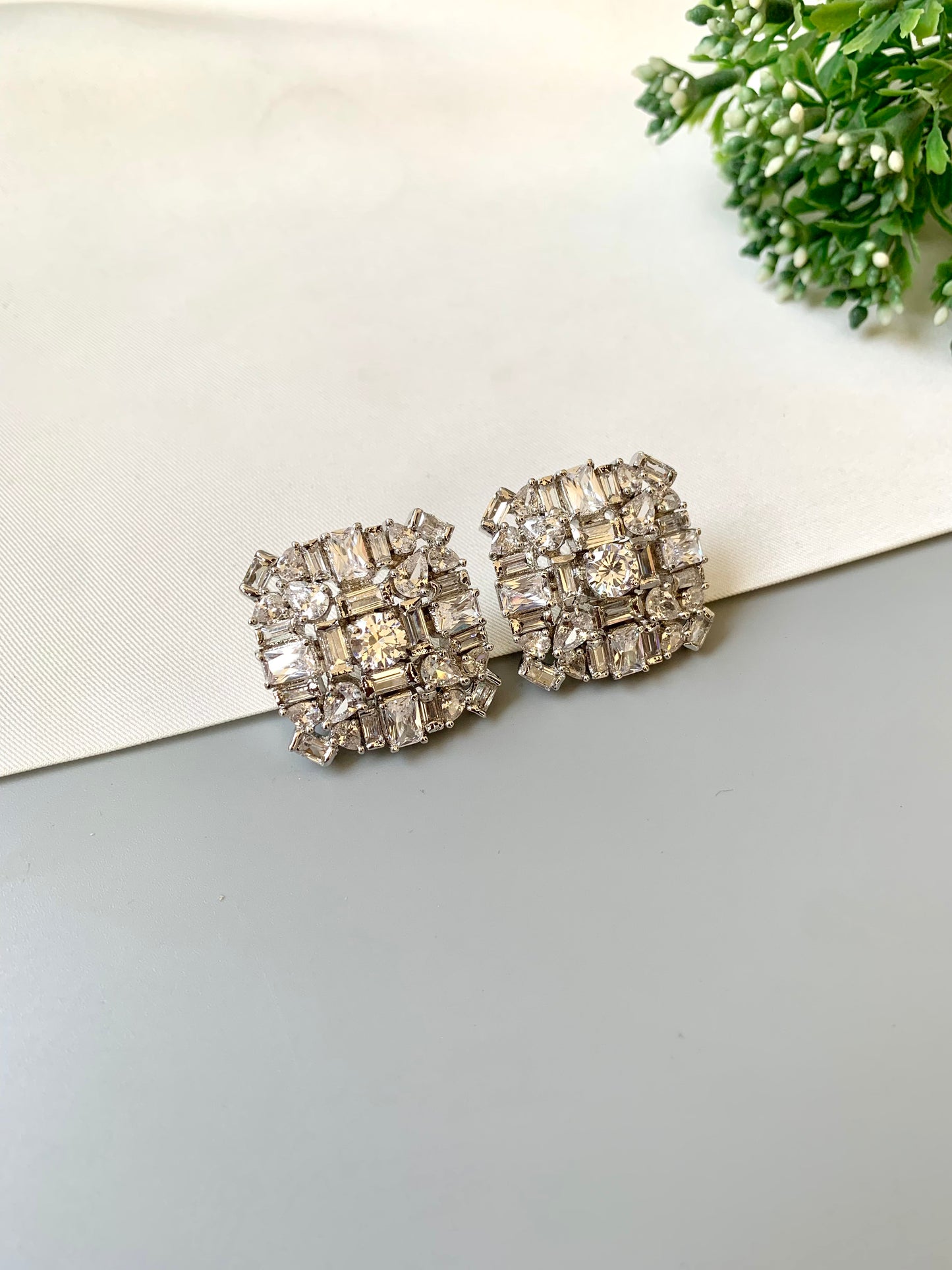 Pair of silver stud earrings with clear stones on a light gray surface.