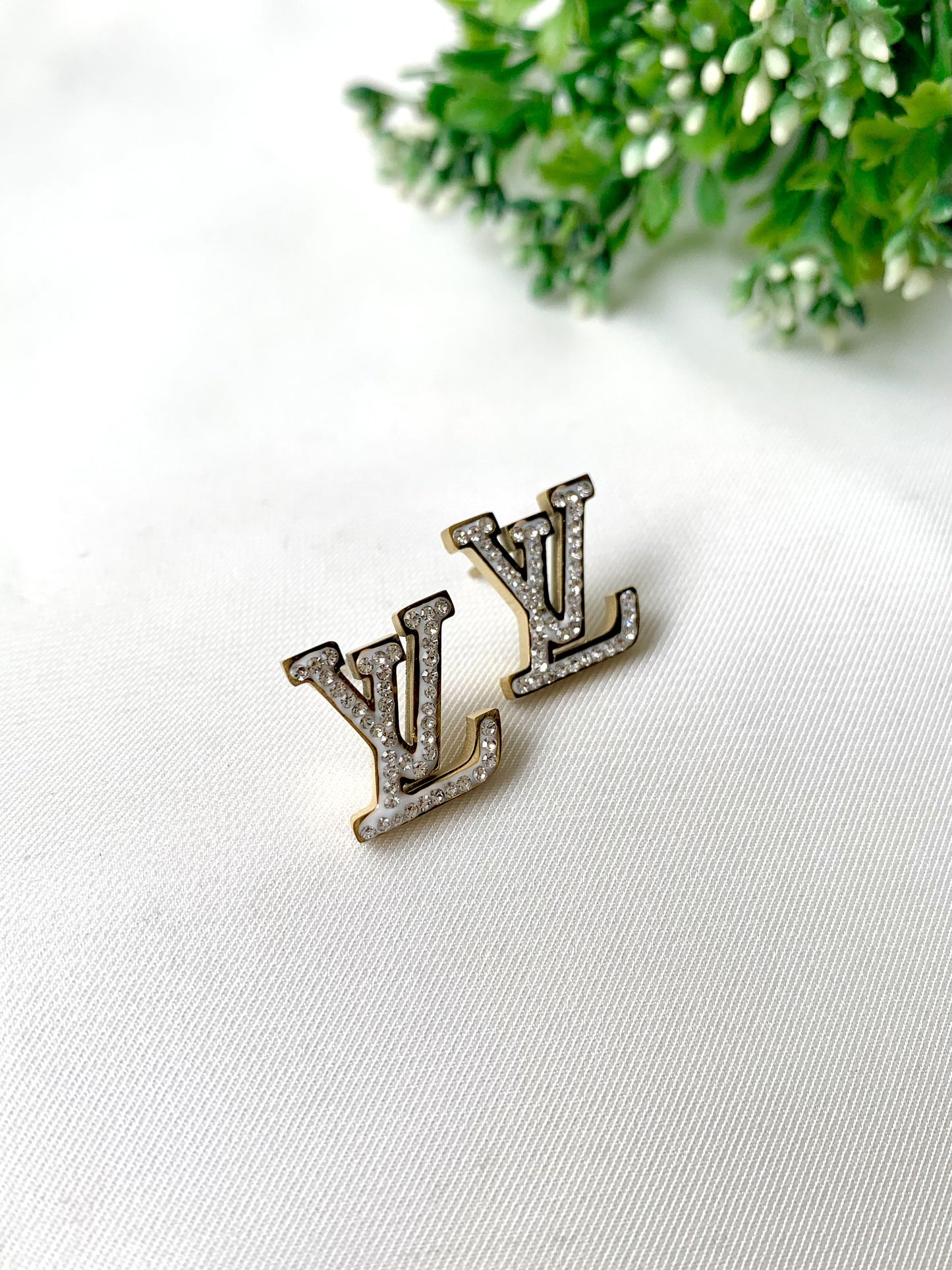 LV-shaped gold stud earrings with white pavé stones and white enamel detailing — Forma Collection by Zamal Jewels