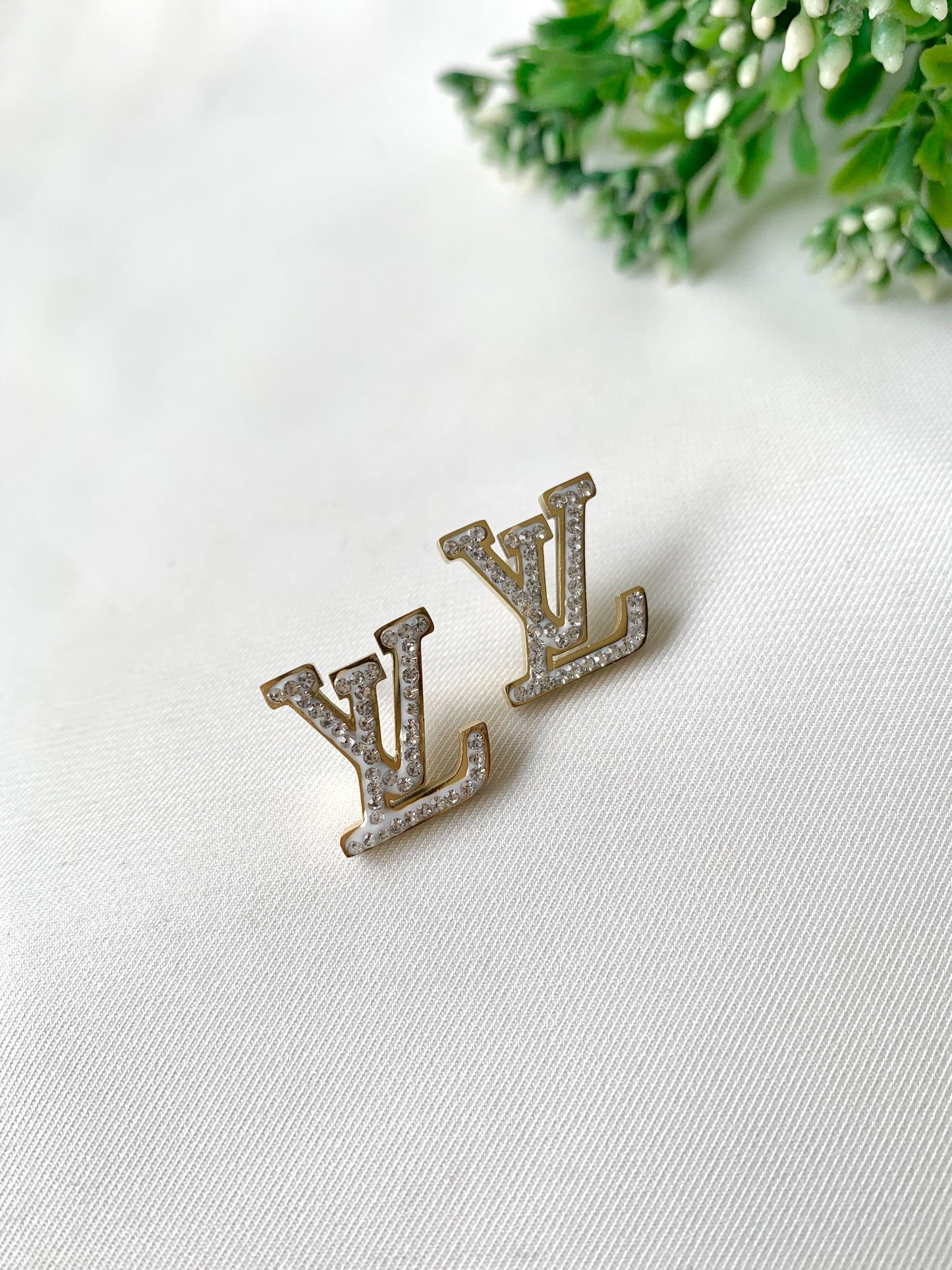 LV-shaped gold stud earrings with white pavé stones and white enamel detailing — Forma Collection by Zamal Jewels