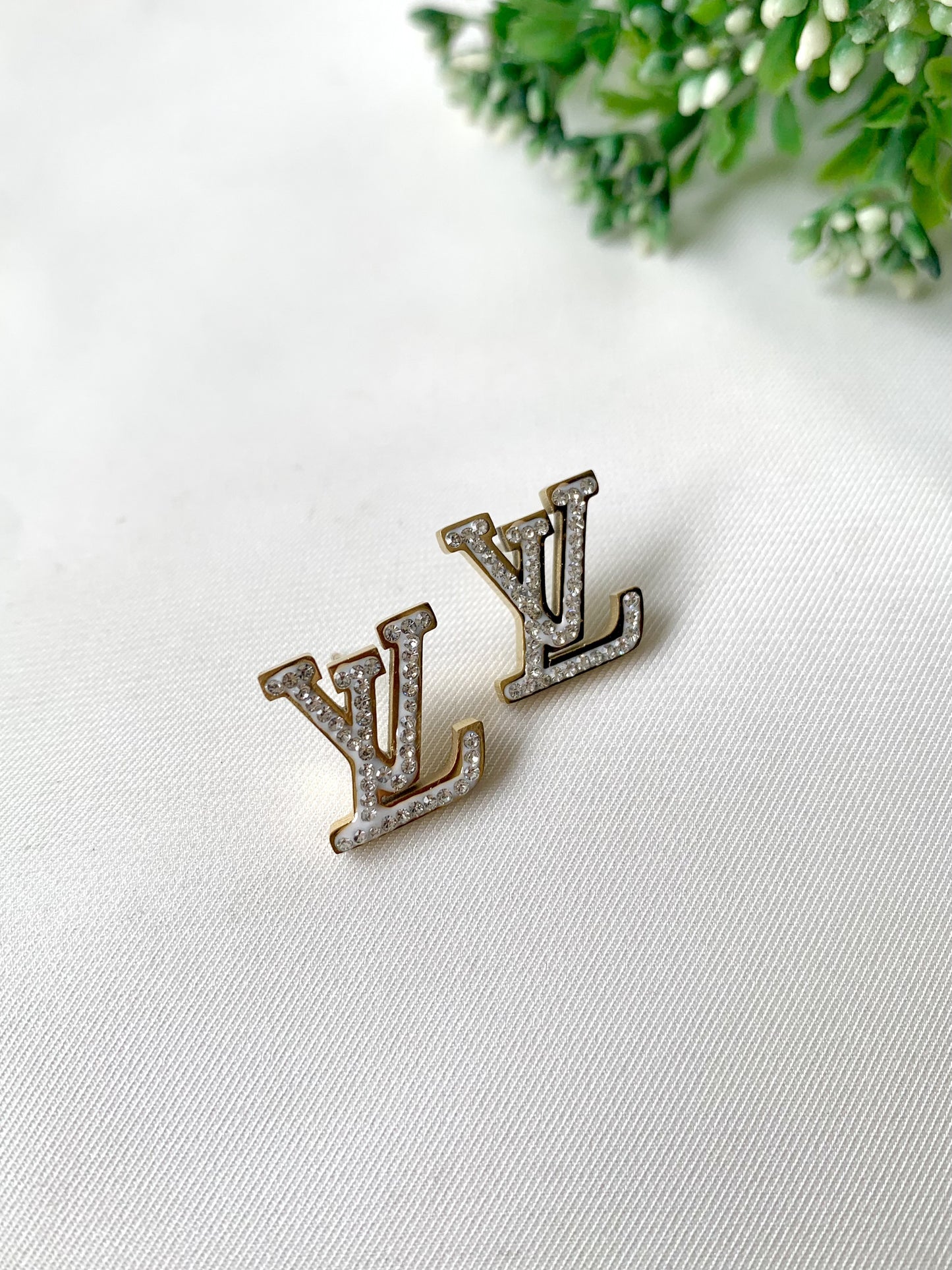 LV-shaped gold stud earrings with white pavé stones and white enamel detailing — Forma Collection by Zamal Jewels