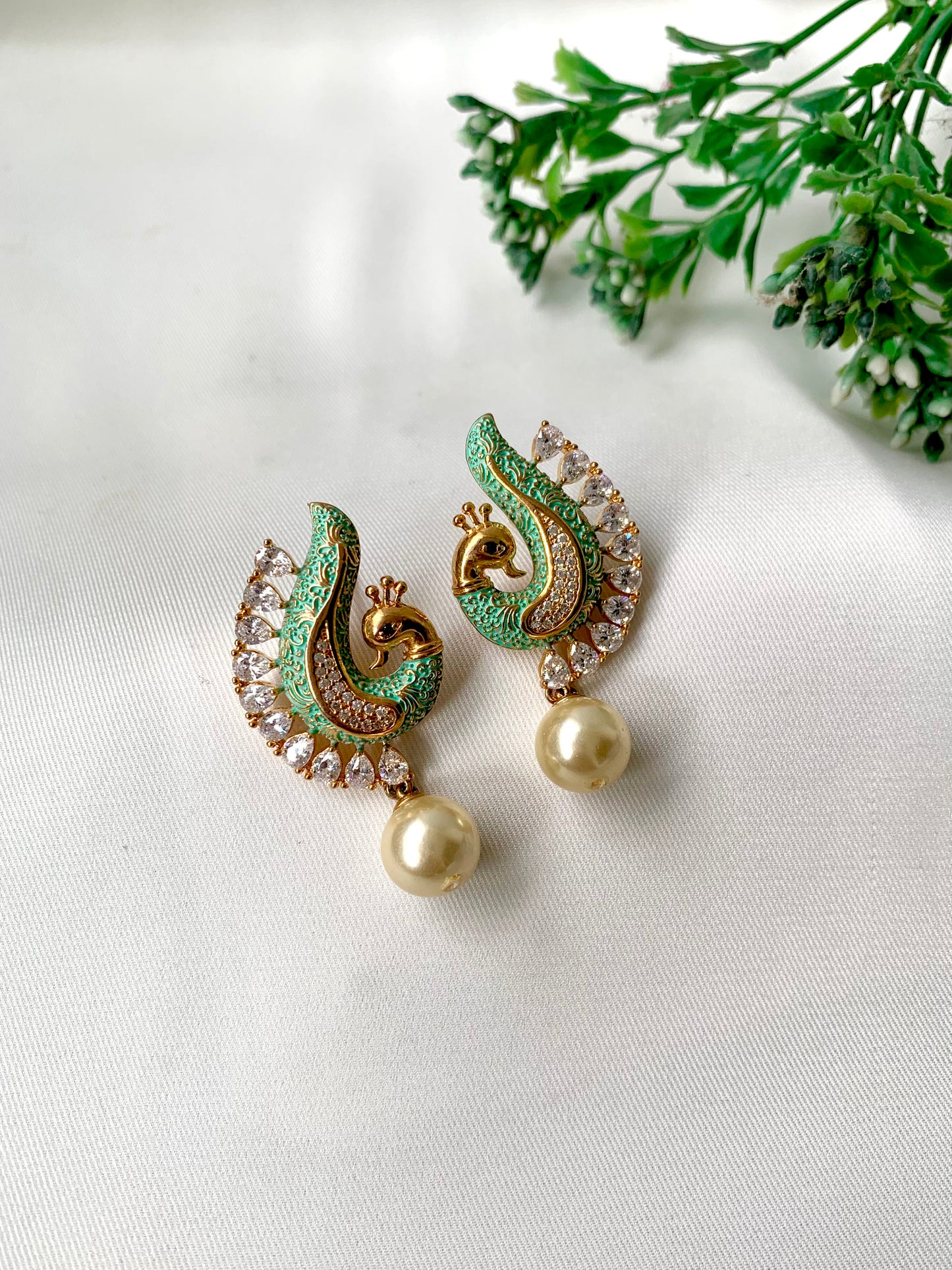 Pair of green and gold earrings with pearl drops on a white background
