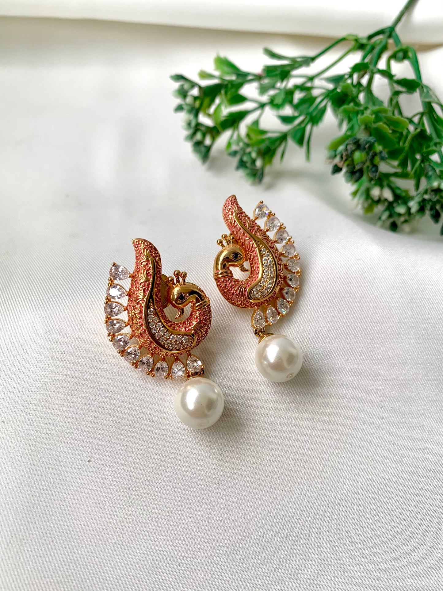 Pair of ornate earrings with pearl drops on a light background