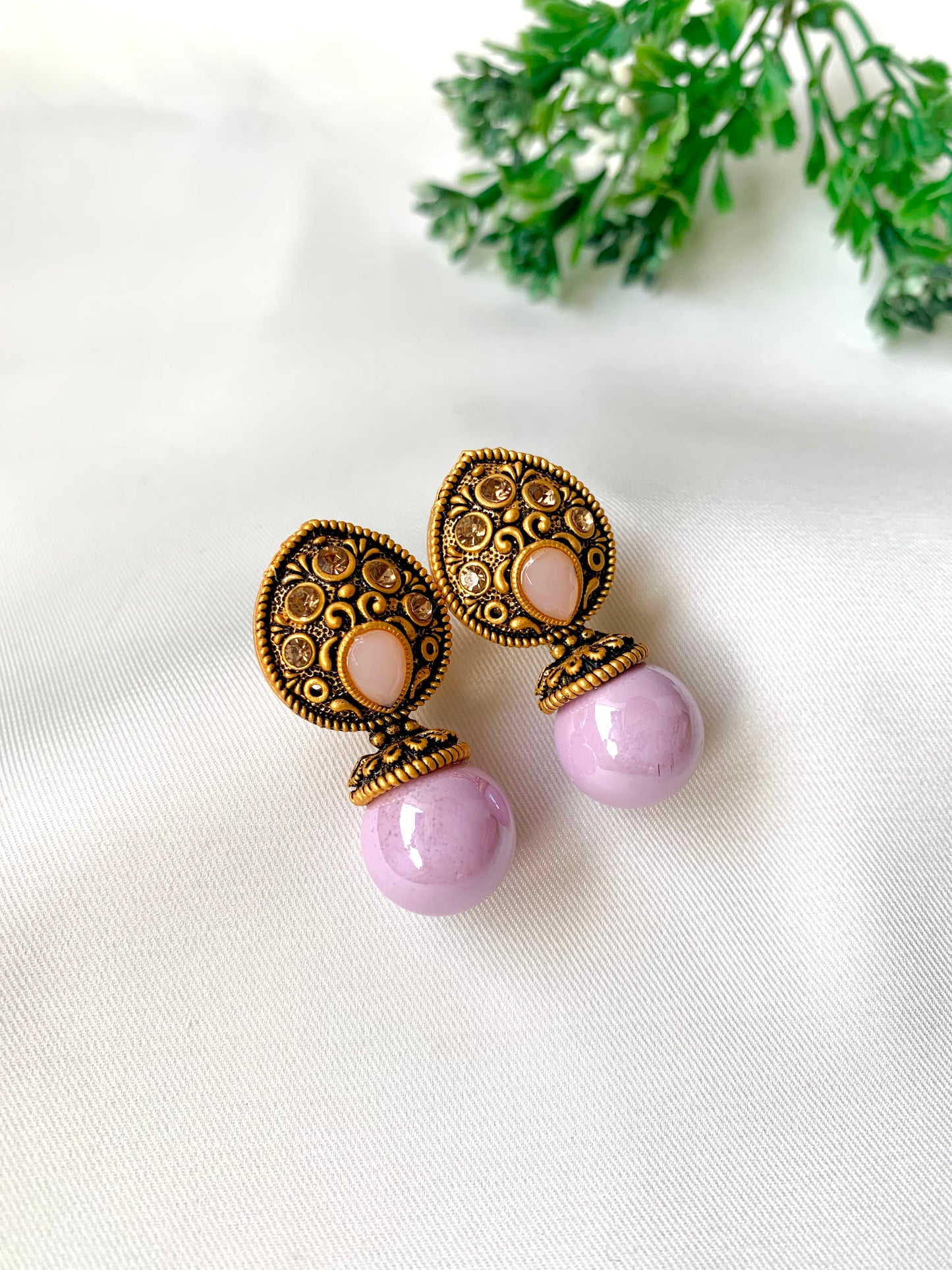Pair of earrings with purple spherical elements and gold intricate designs on a white background.