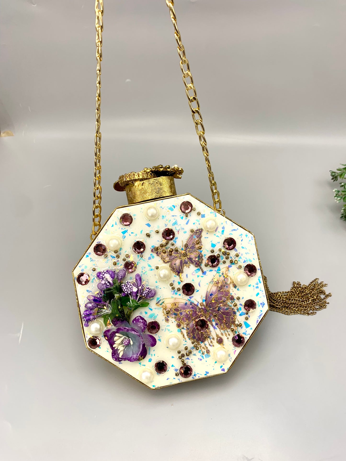 Decorative hexagonal pendant with floral elements and a gold chain on a light gray background