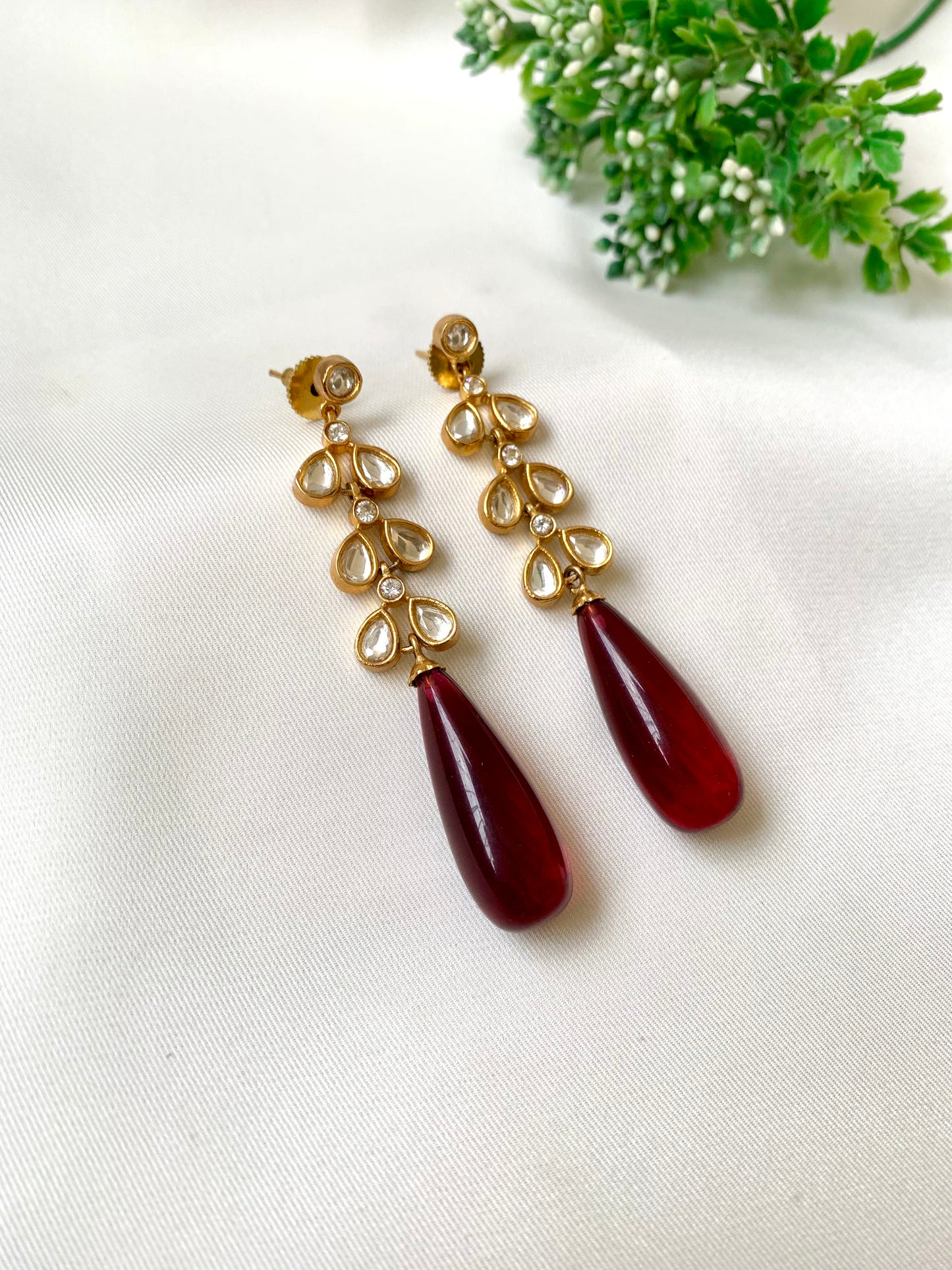 Gold earrings with red teardrop-shaped stones on a white background