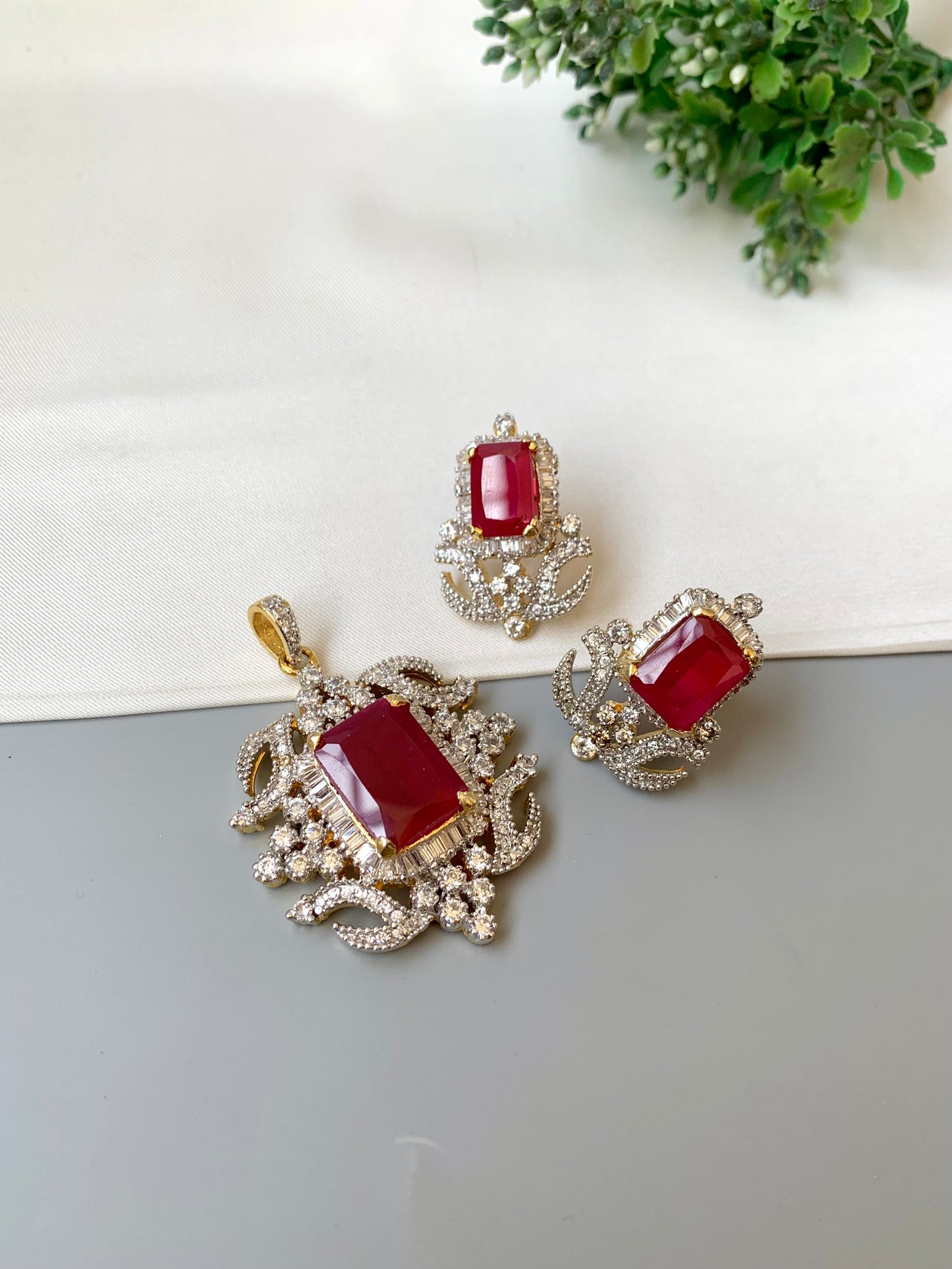 Jewelry set with red gemstones and gold accents on a white surface with greenery.