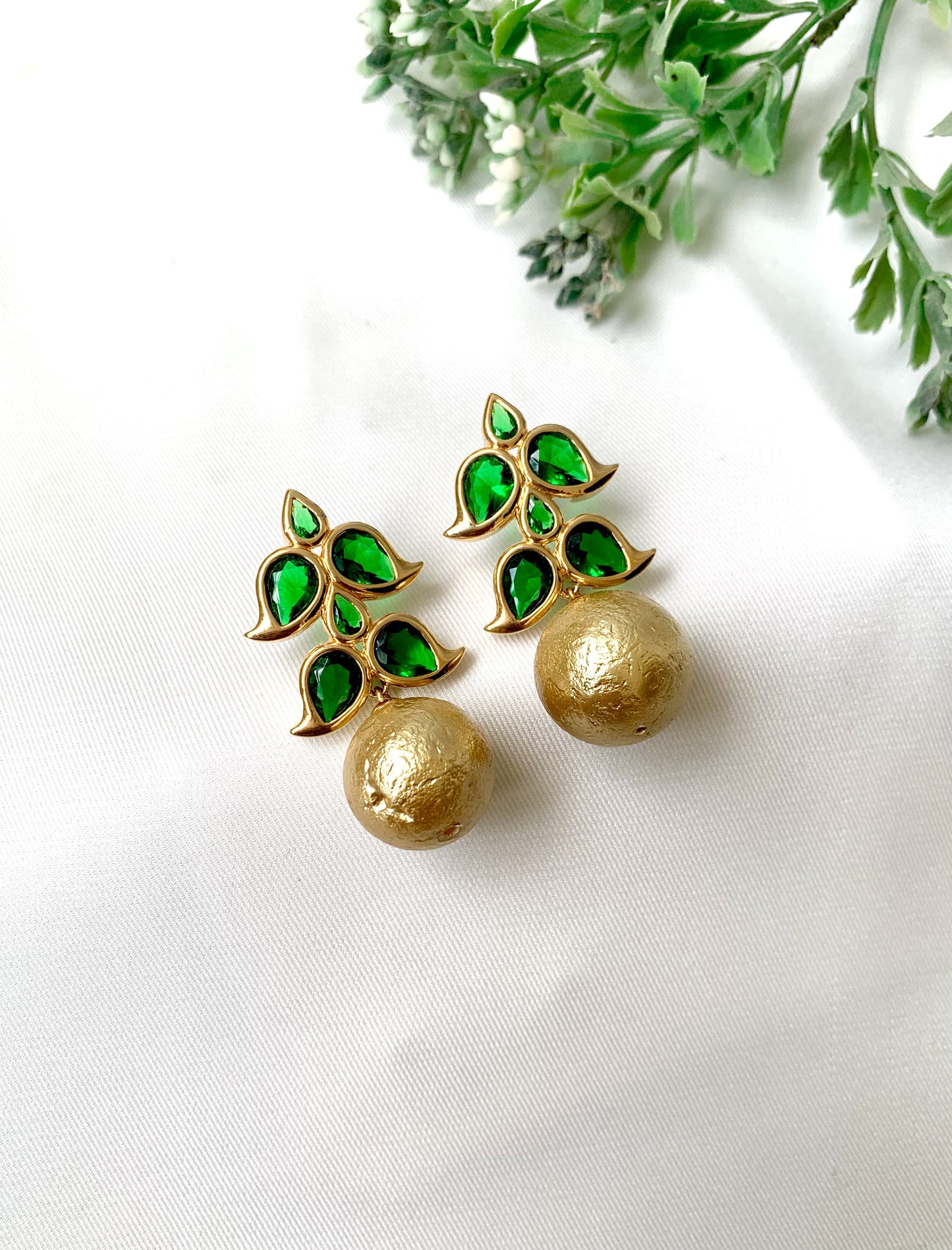 Gold earrings with green gemstones on a white background