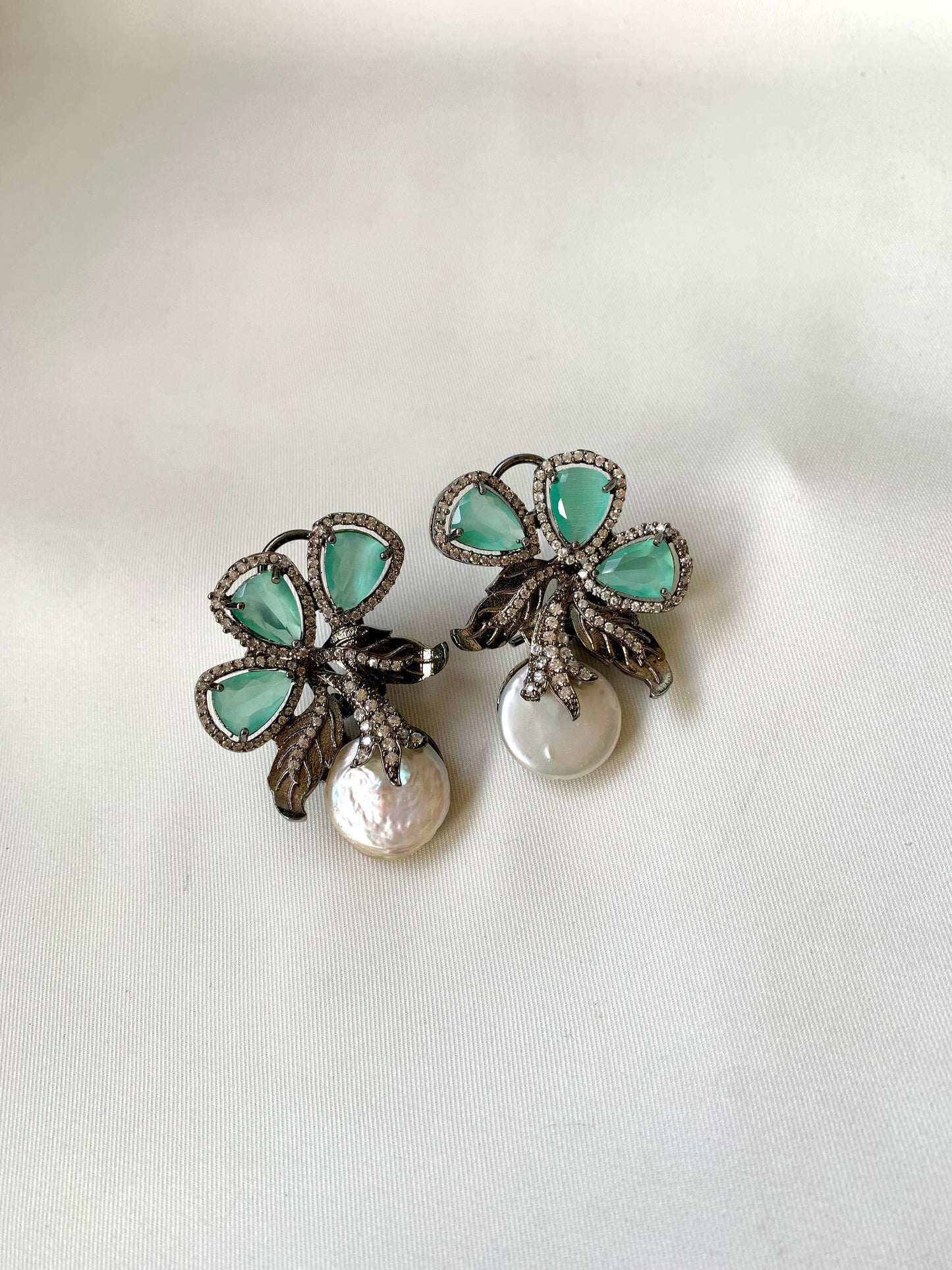 Pair of earrings with green gemstones and a pearl on a white background