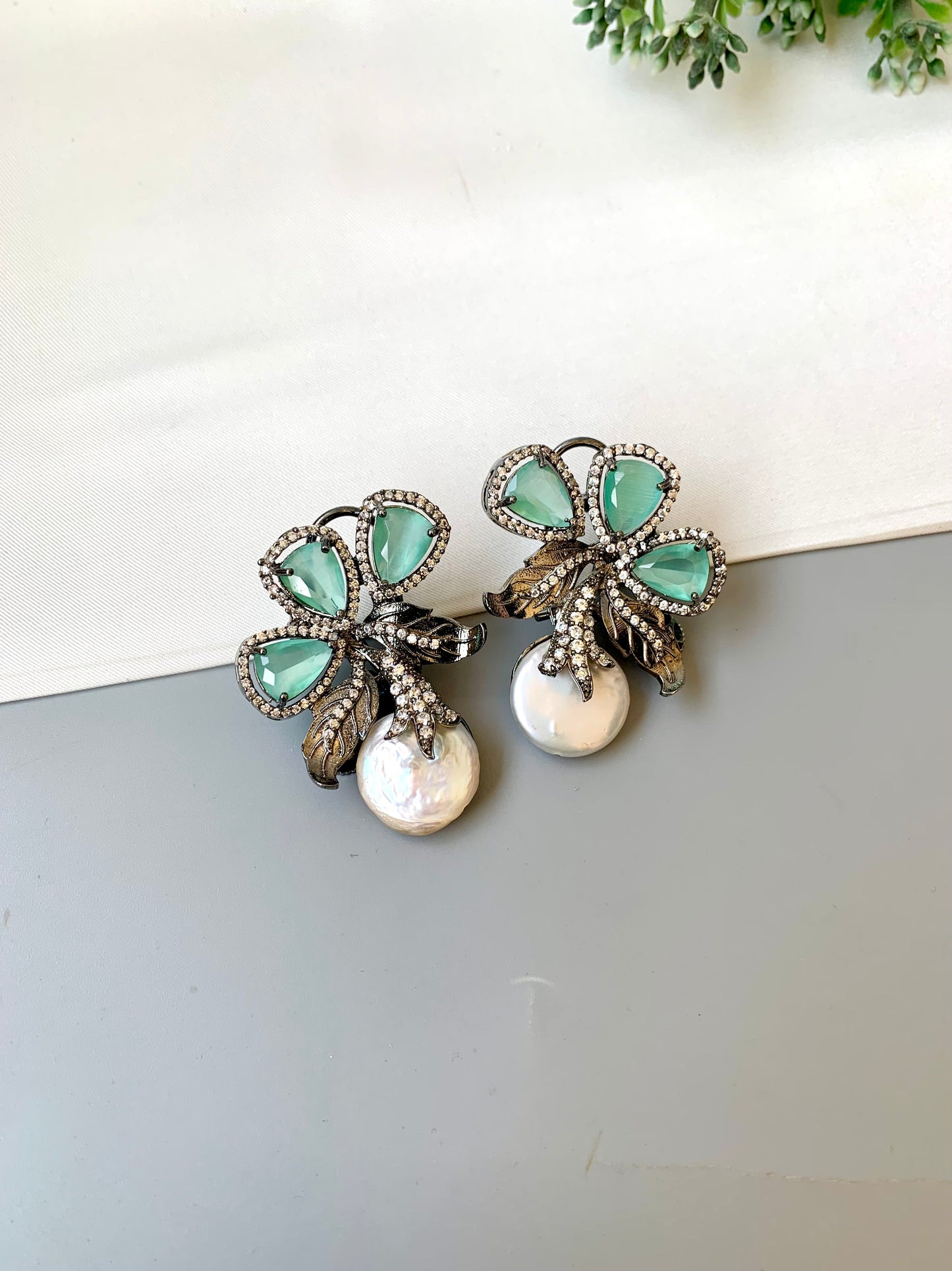 Pair of earrings with green gemstones and pearl-like elements on a white surface.