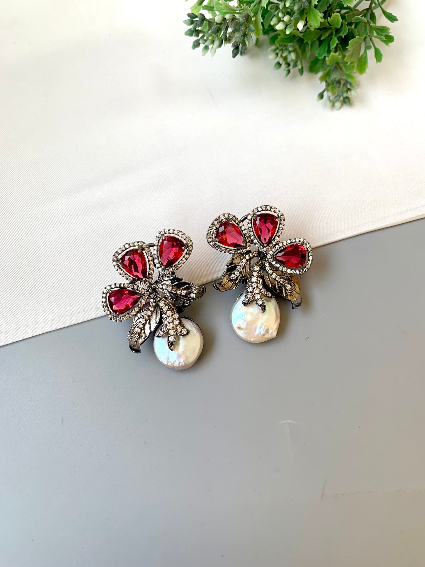 Pair of earrings with red gemstones and pearl-like centers on a light surface.
