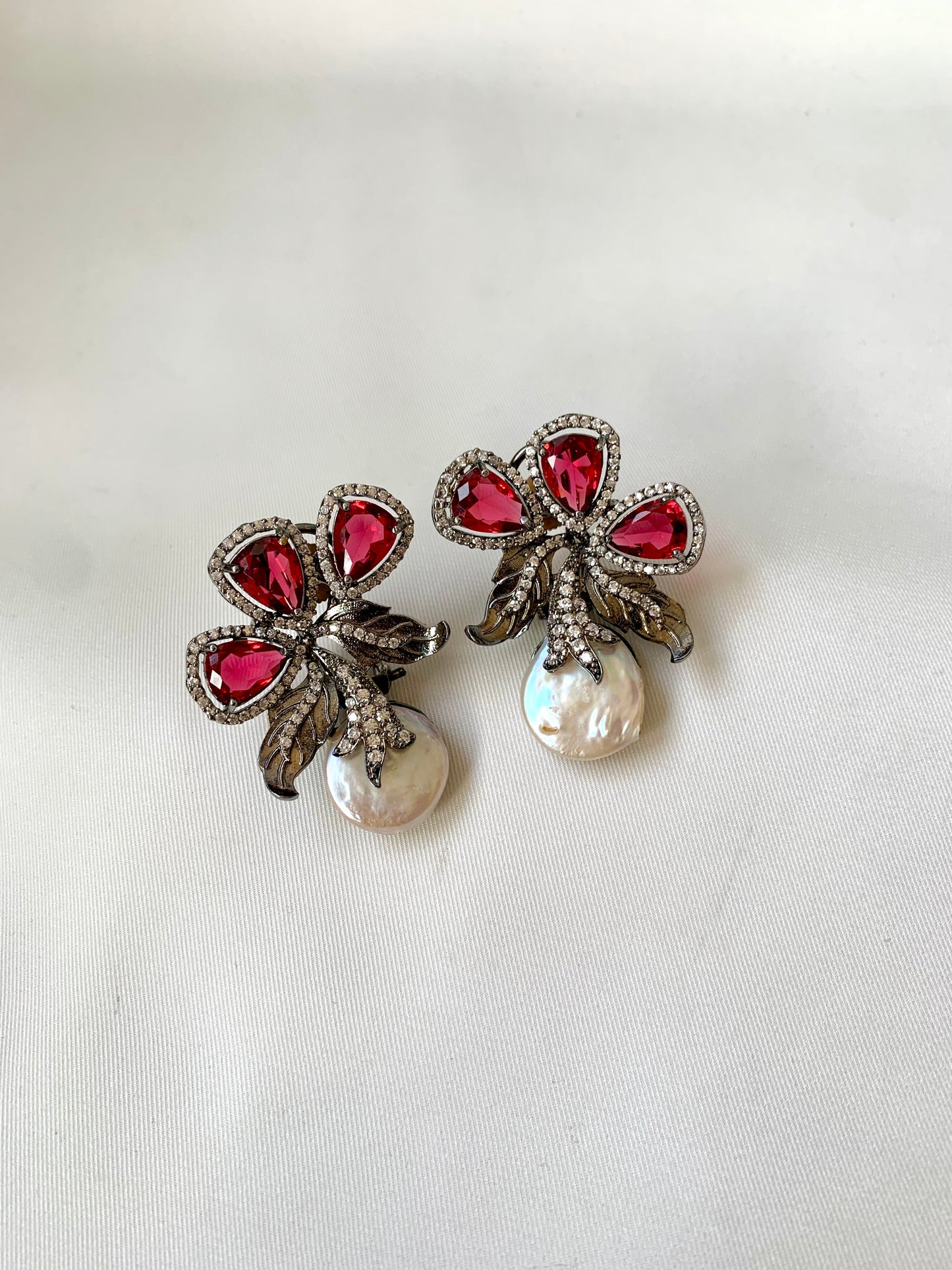 Pair of earrings with red gemstones and pearl-like centers on a white background