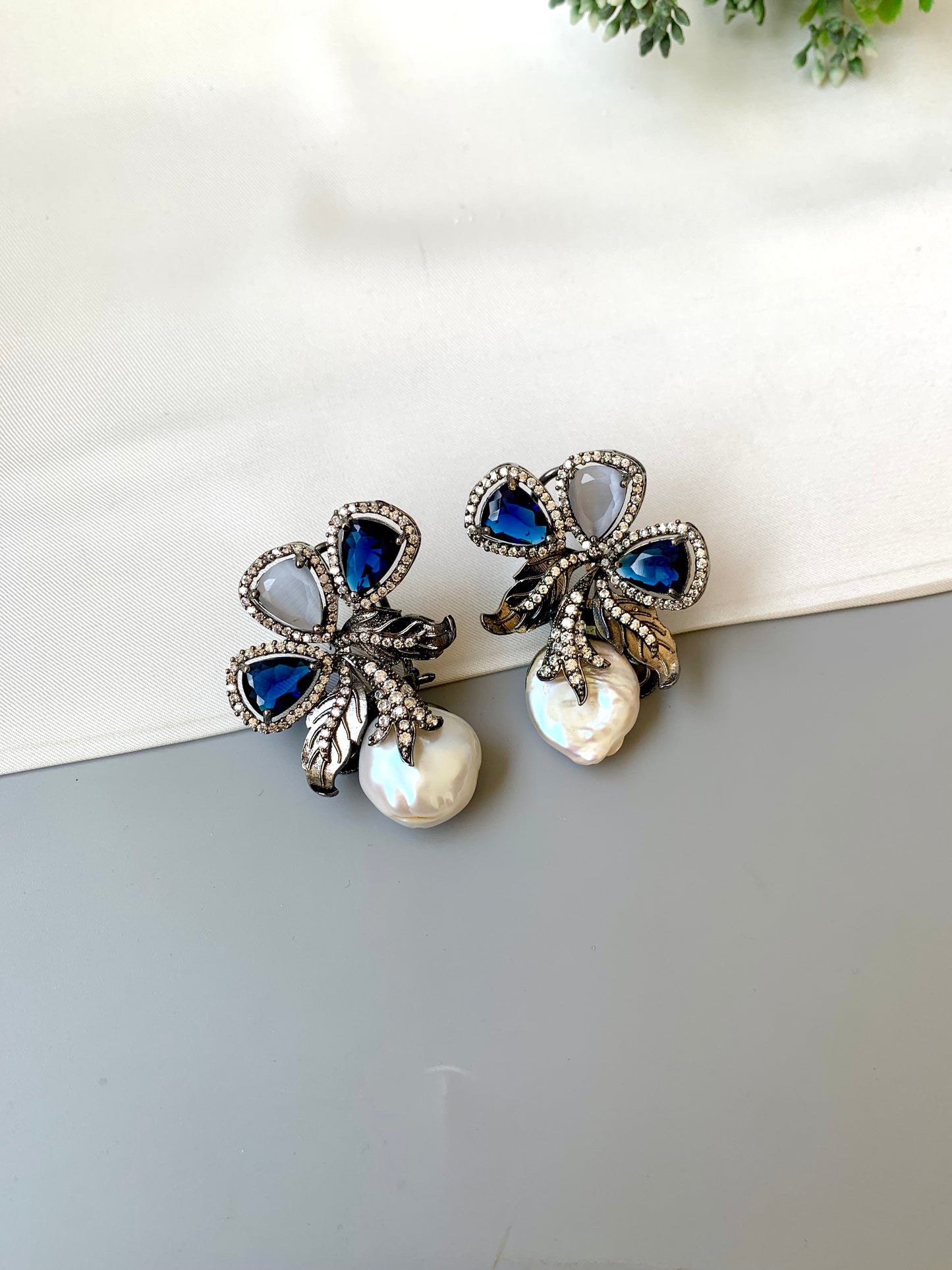 Pair of decorative earrings with blue stones and pearls on a white surface.