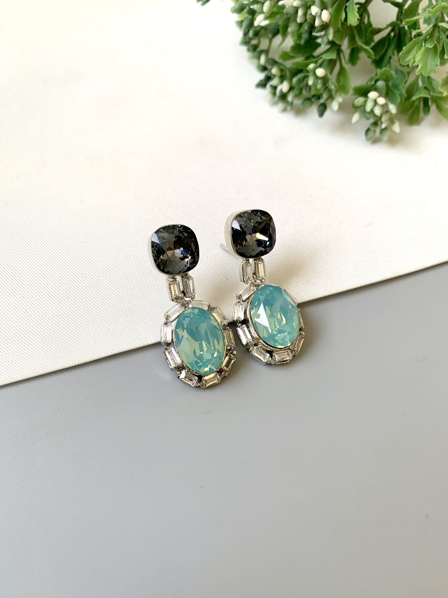 Pair of earrings with black and turquoise stones on a light gray surface with greenery in the background.