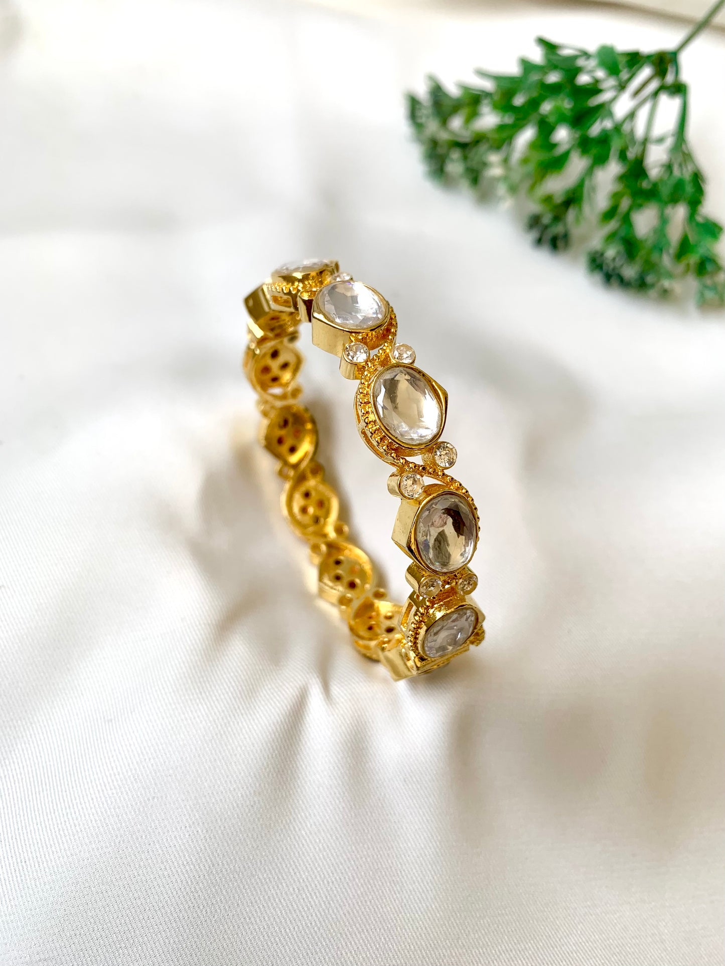 Gold bracelet with clear stones on a white fabric background