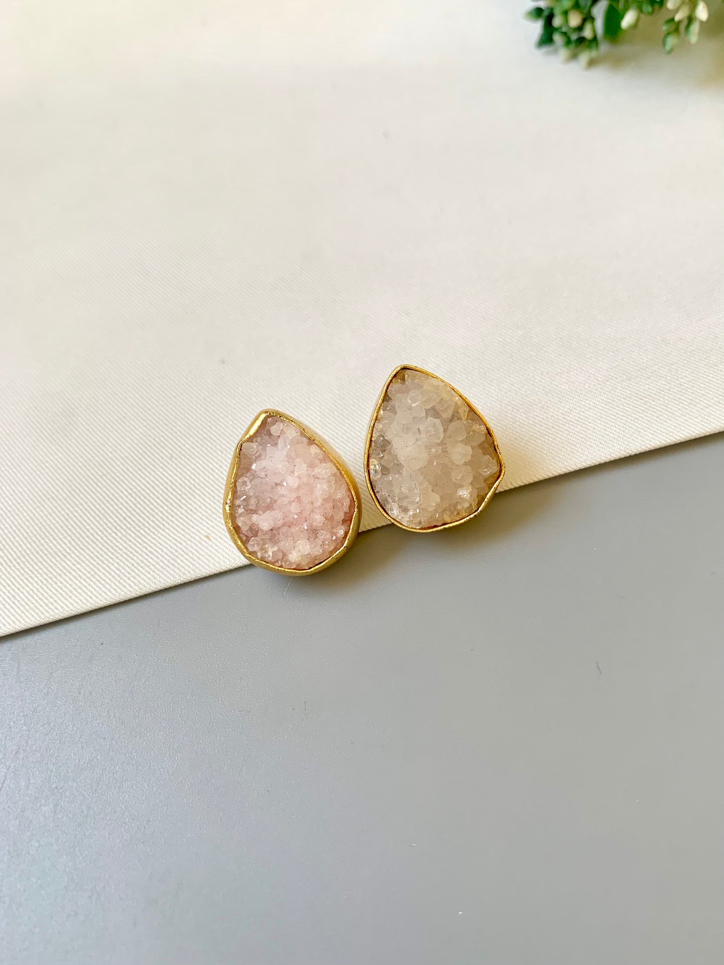 Teardrop-shaped earrings with gold rims on a light gray surface.