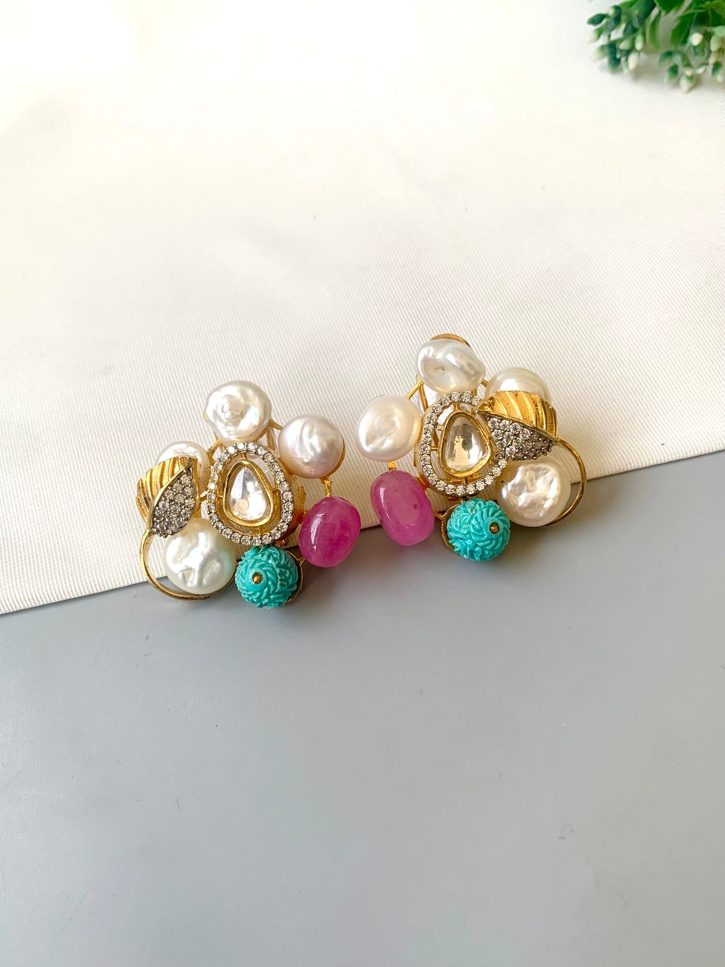 Pair of decorative earrings with pearls and colorful beads on a white surface.