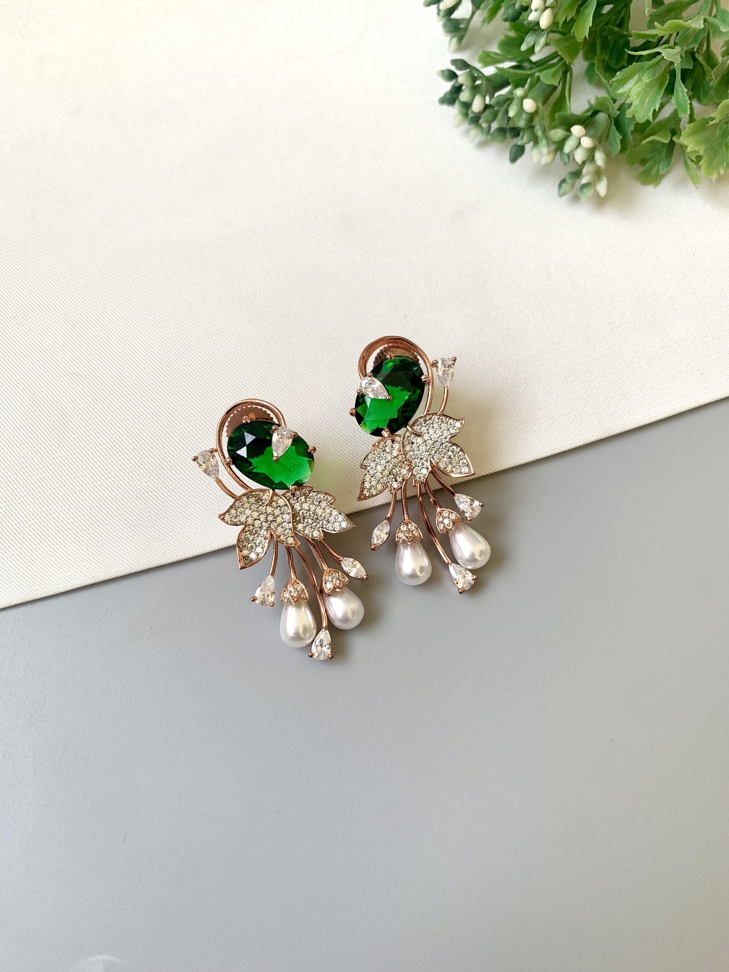 Earrings with green gemstones and pearl-like elements on a light background