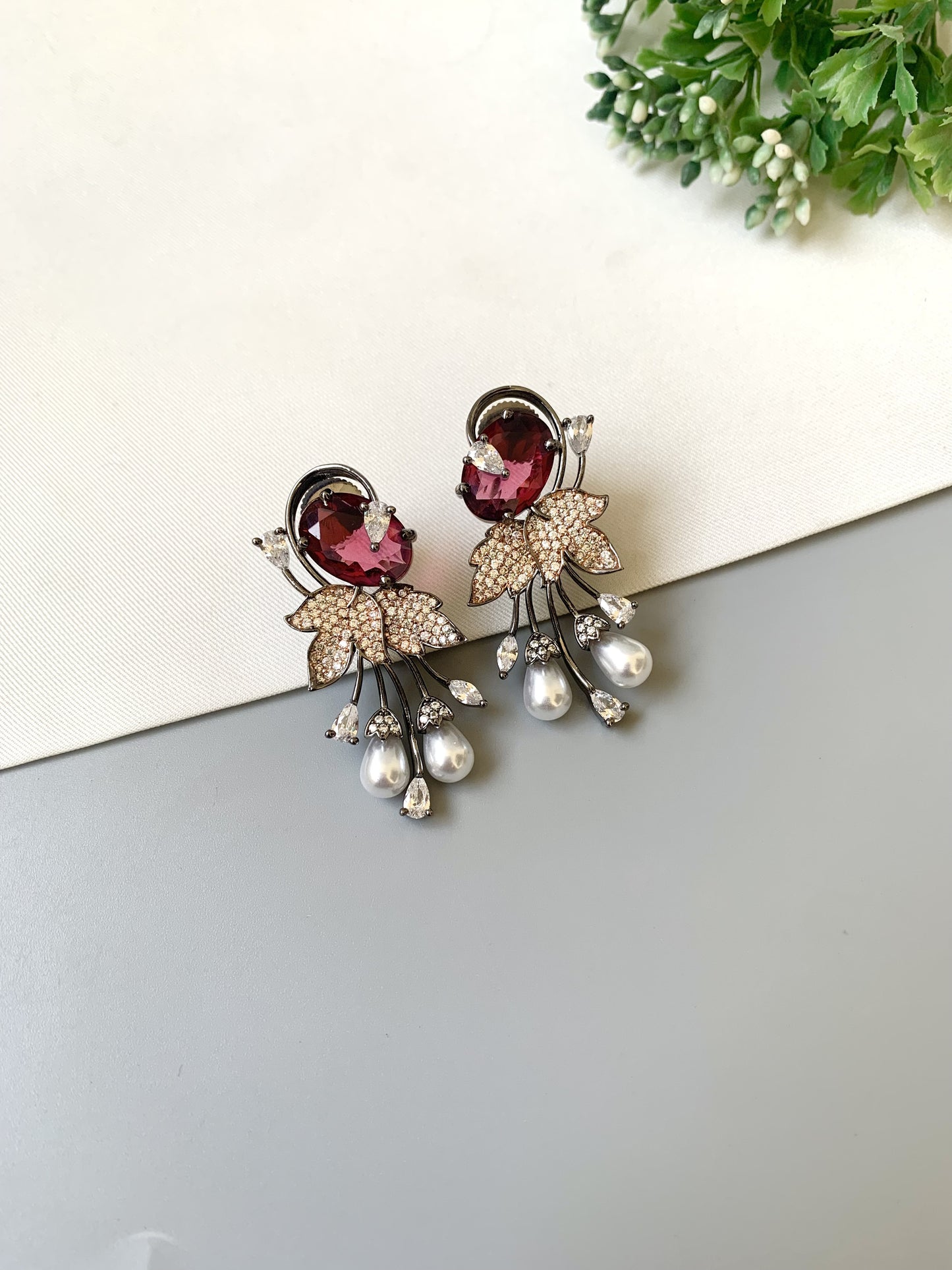 Pair of decorative earrings with gemstones and pearls on a light surface.