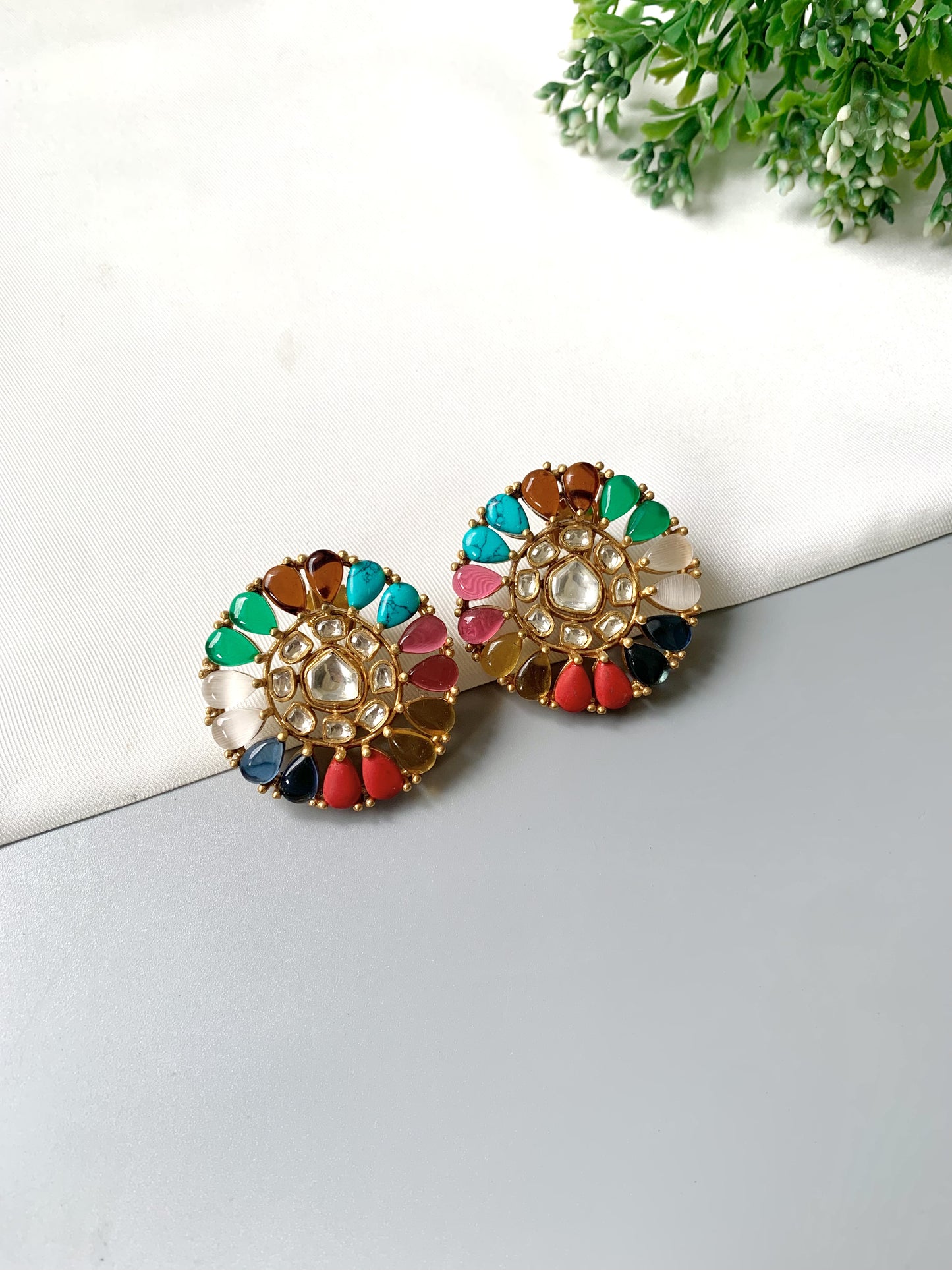 Multicolored earrings on a white surface with greenery in the background