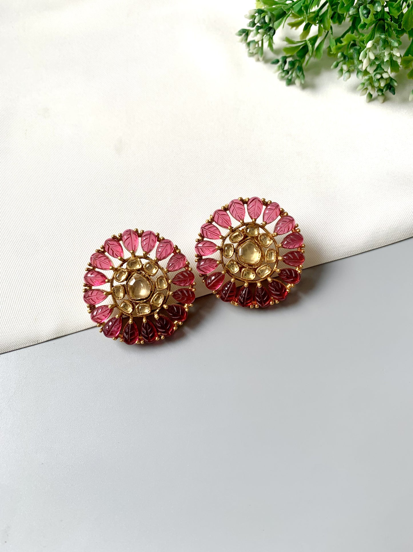 Pair of gold and pink earrings on a white surface with greenery in the background