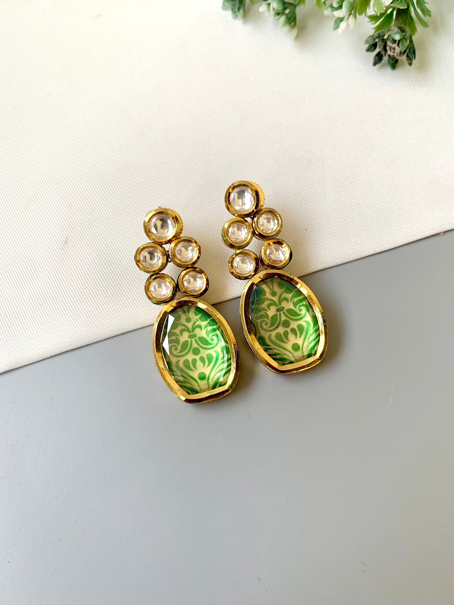 Green earrings with gold accents on a light gray surface