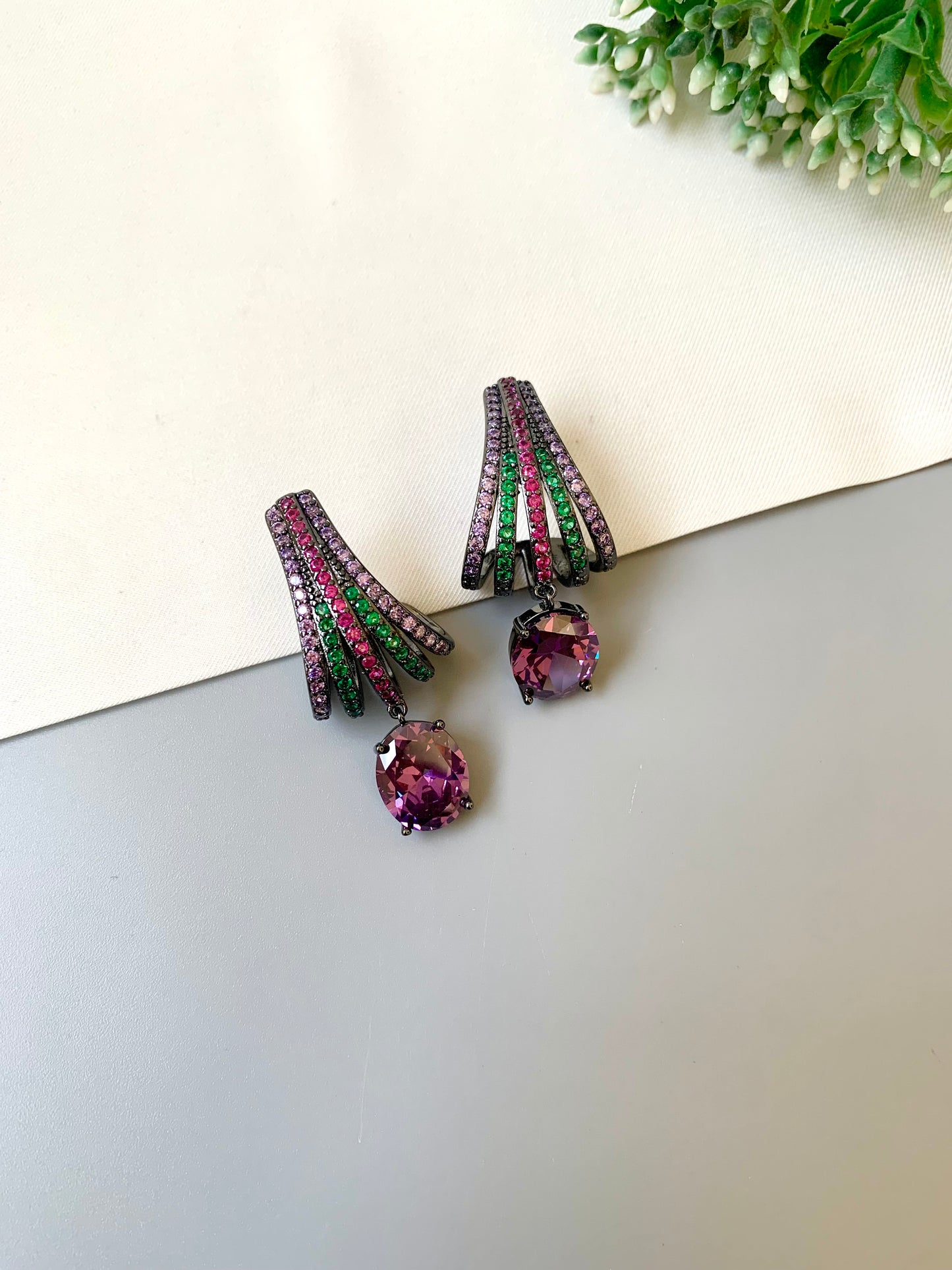 Pair of purple gemstone earrings on a light surface with greenery in the background