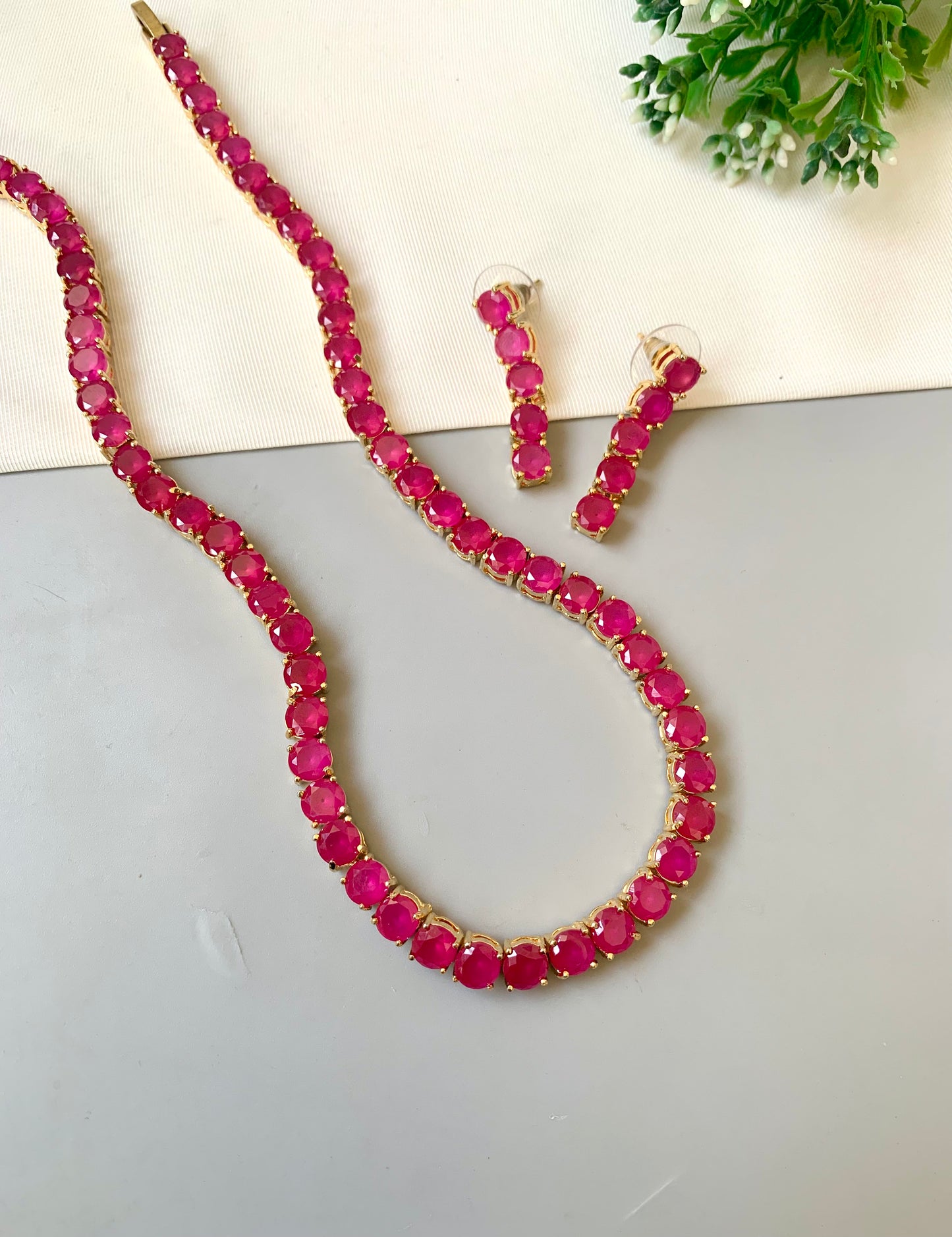Necklace and earrings with red gemstones on a light gray surface.