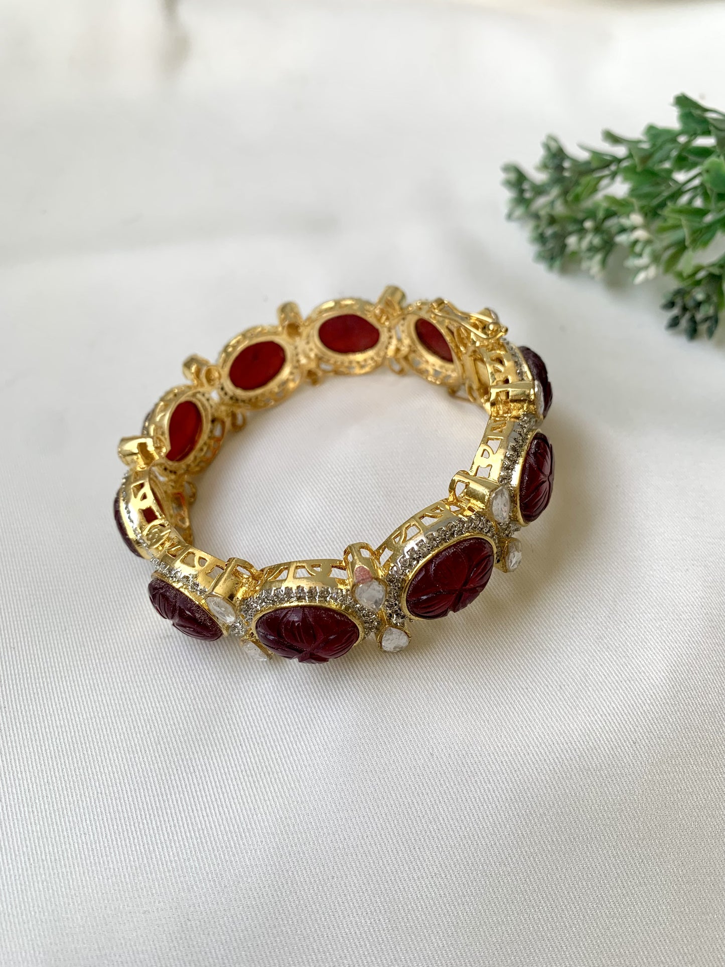 Gold bracelet with red stones on a white fabric background