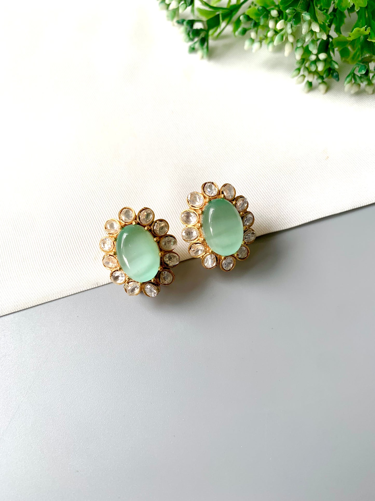 Pair of earrings with green gemstones on a white surface with greenery in the background
