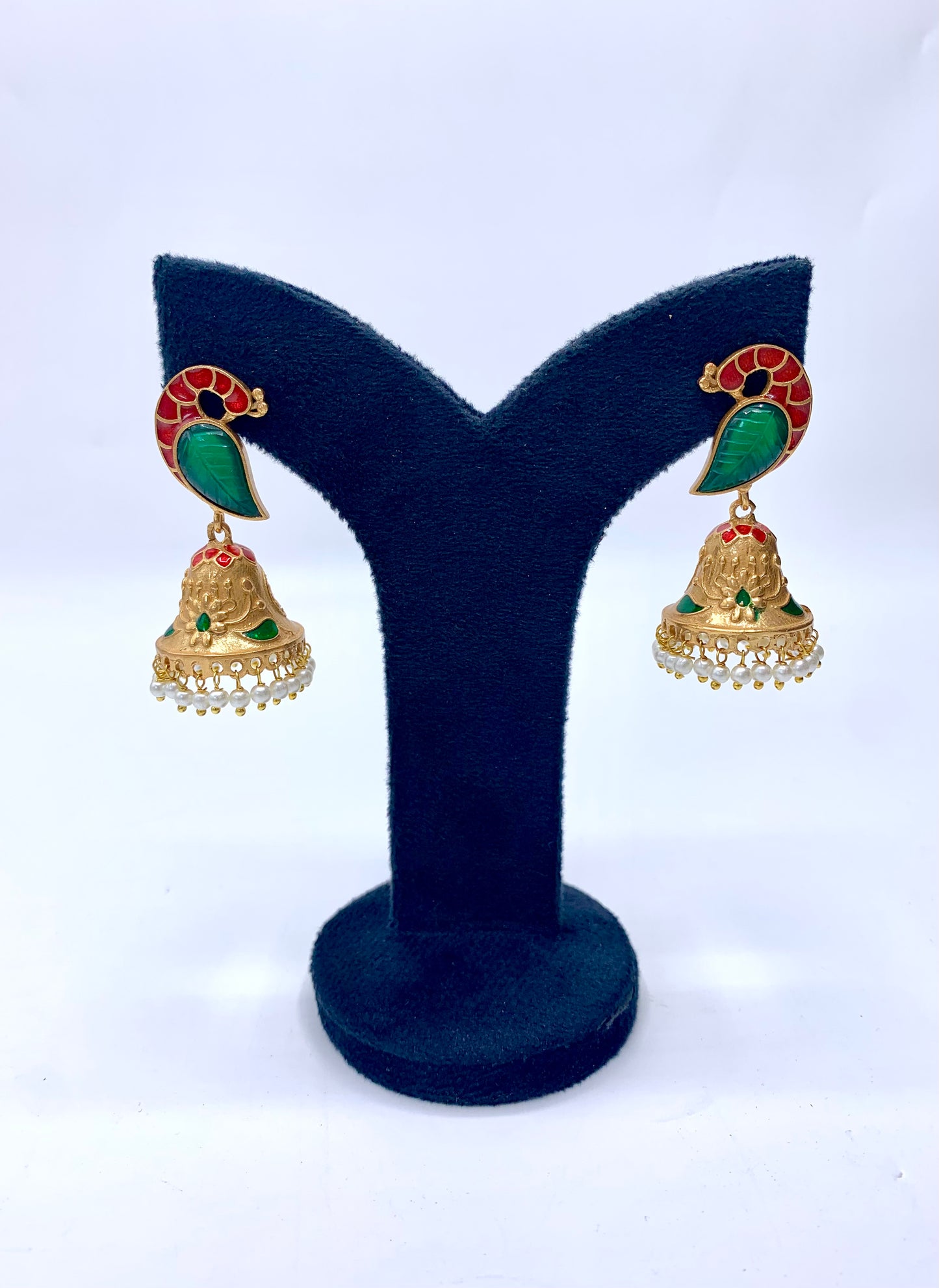 A pair of gold-plated earrings with green and red stone accents and white pearl drops, displayed on a black stand.